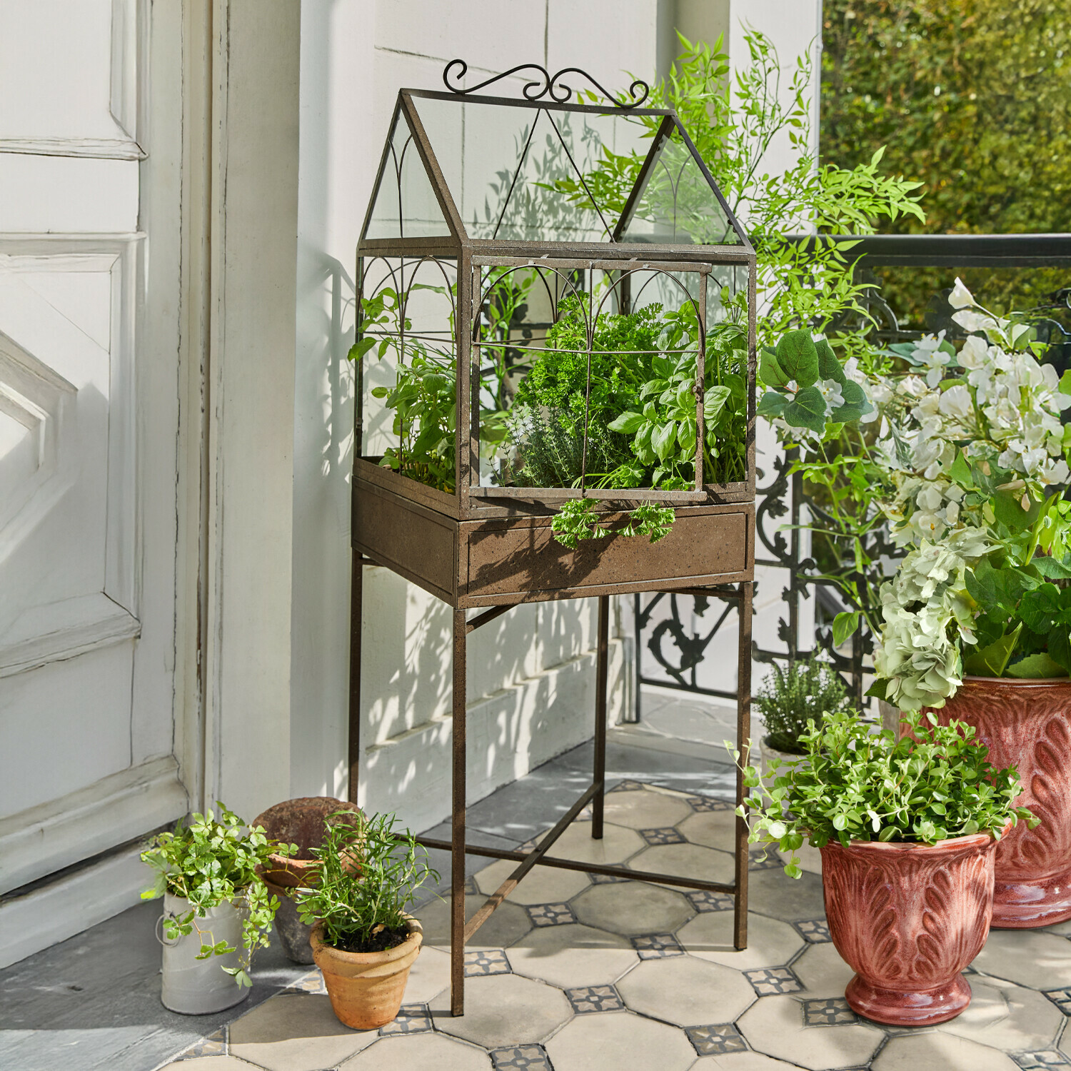 Kovová skleník s rezavou patinou na stojanu s bylinkami na dlažbě na terase