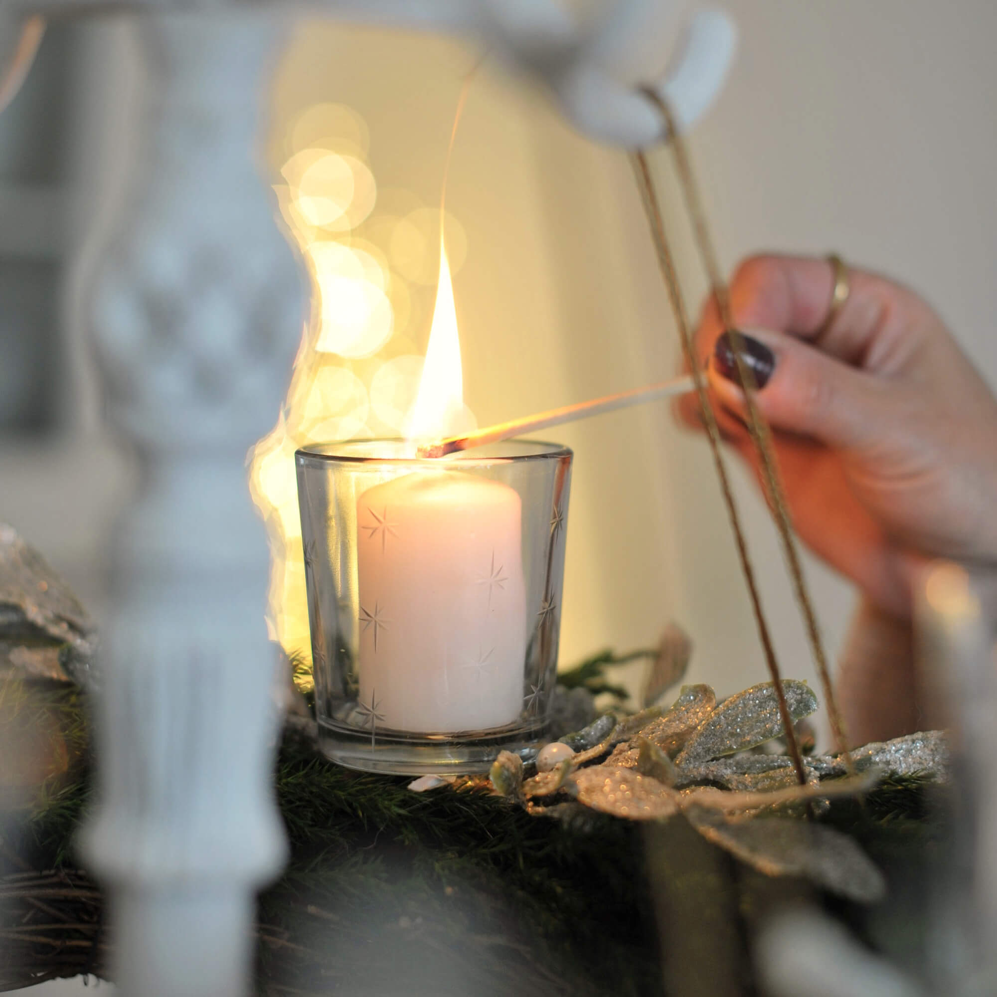 Bílá svíčka ve skleněném svícnu na zeleném adventním věnci s třpytivou dekorací