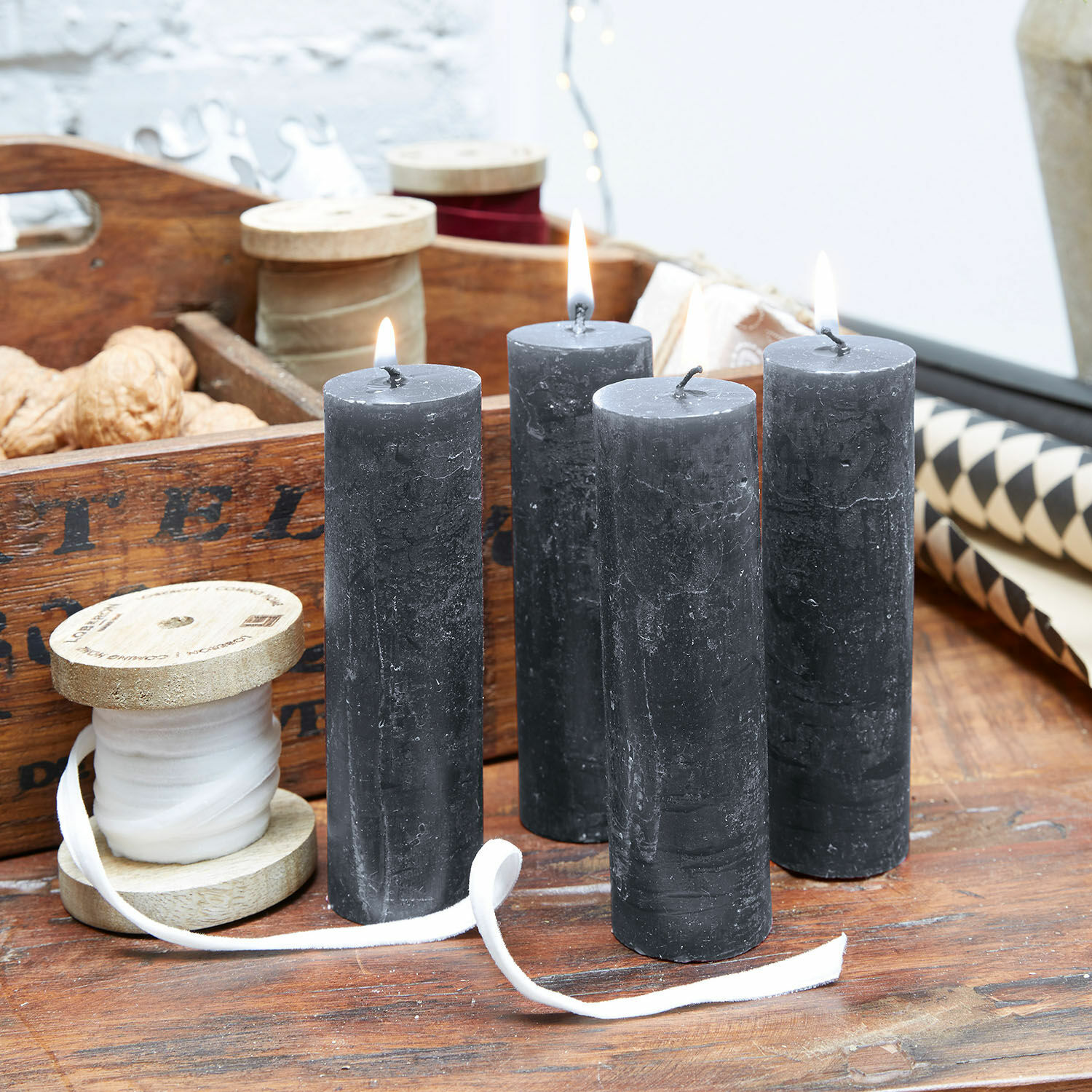 Čtyři černé svíčky z přírodního vosku na dřevěném stole s dekorativními cívkami a ořechy