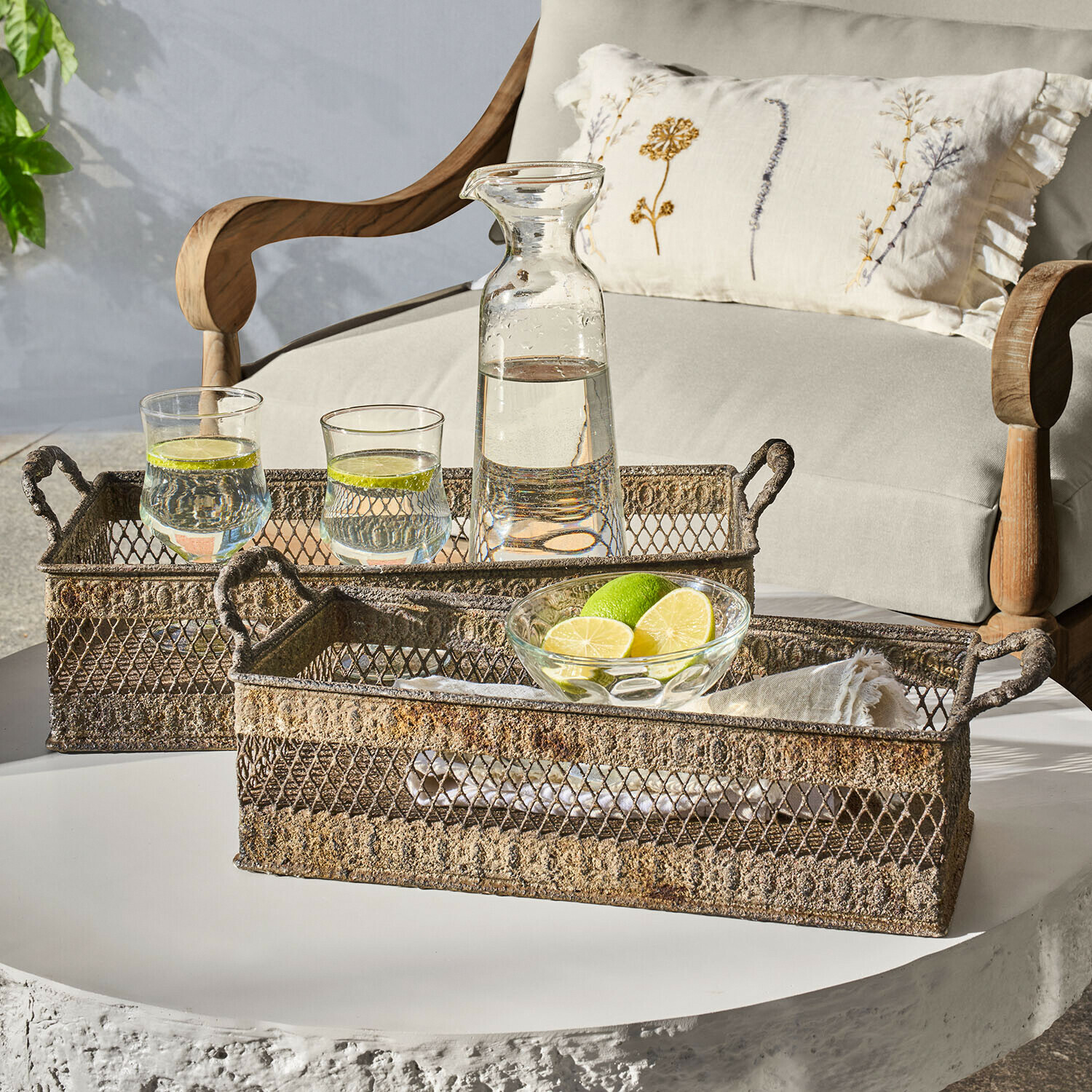 Dva rustikální kovové podnosy s úchyty na bílém stole s karafou a sklenicemi vody s limetkou