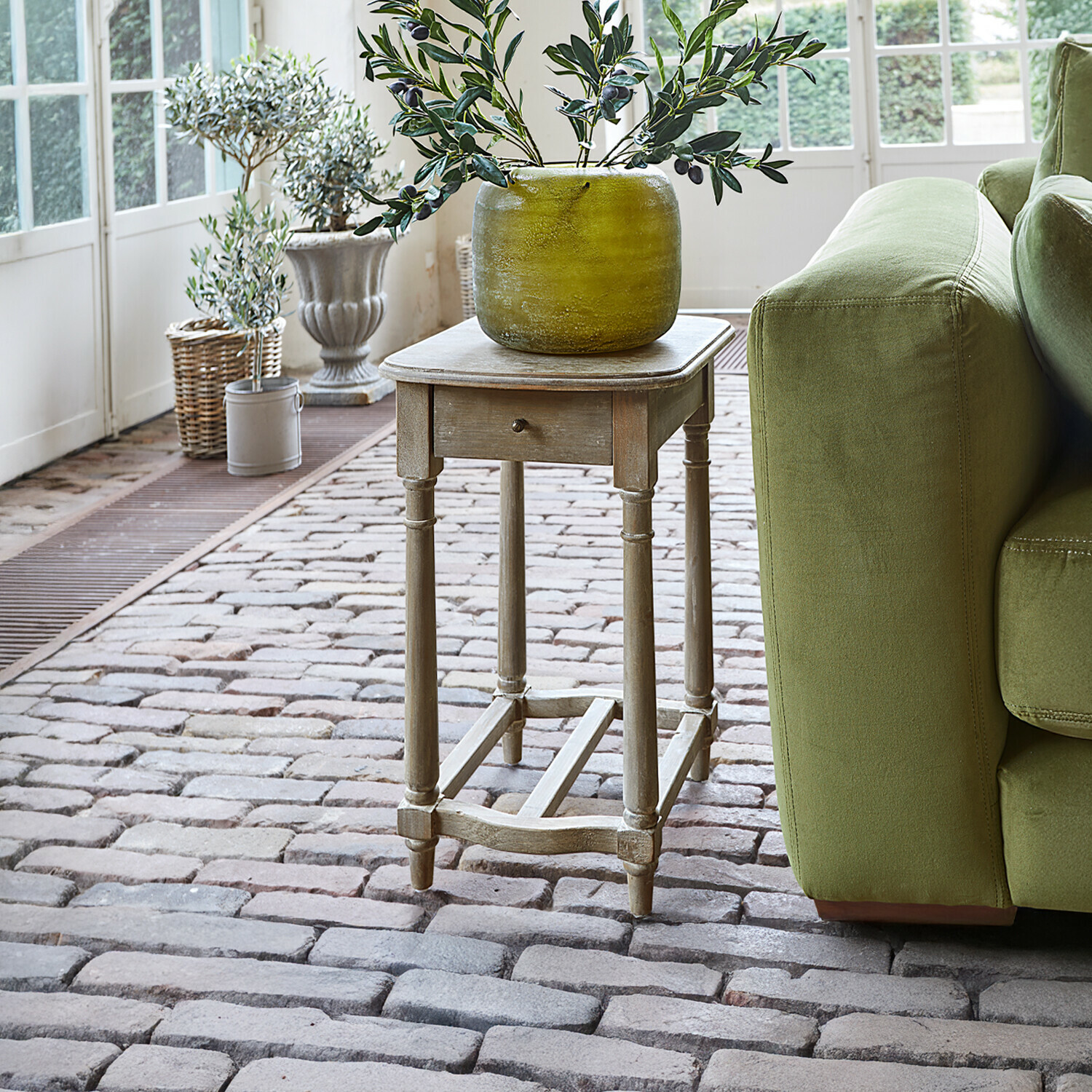 Odkládací stolek Jaxeno Dřevěný vintage odkládací stolek se zásuvkou a zelenou dekorativní vázu na cihlové podlaze