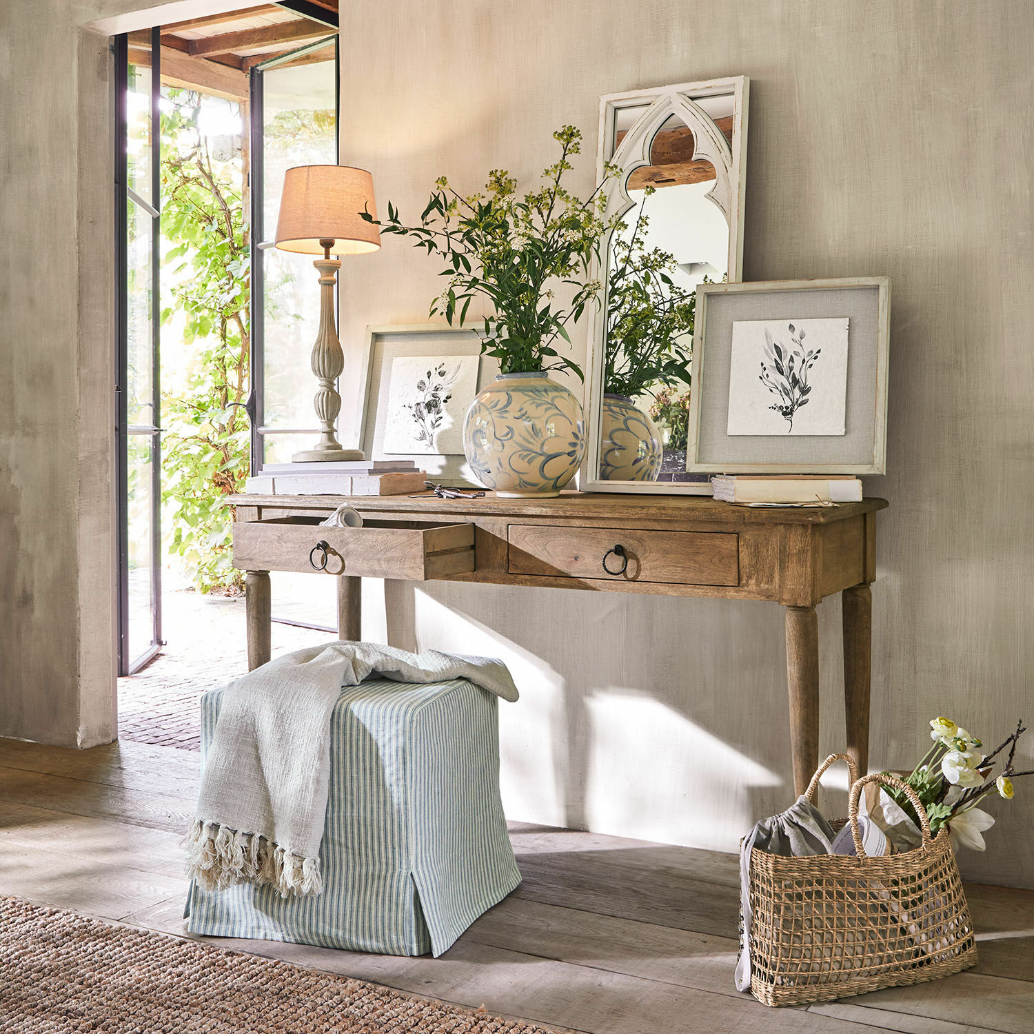 Konzolový stolek Jovrac Dřevěný psací stůl se dvěma zásuvkami, dekorativní zrcadlo a váza s květinami v světlém interiéru