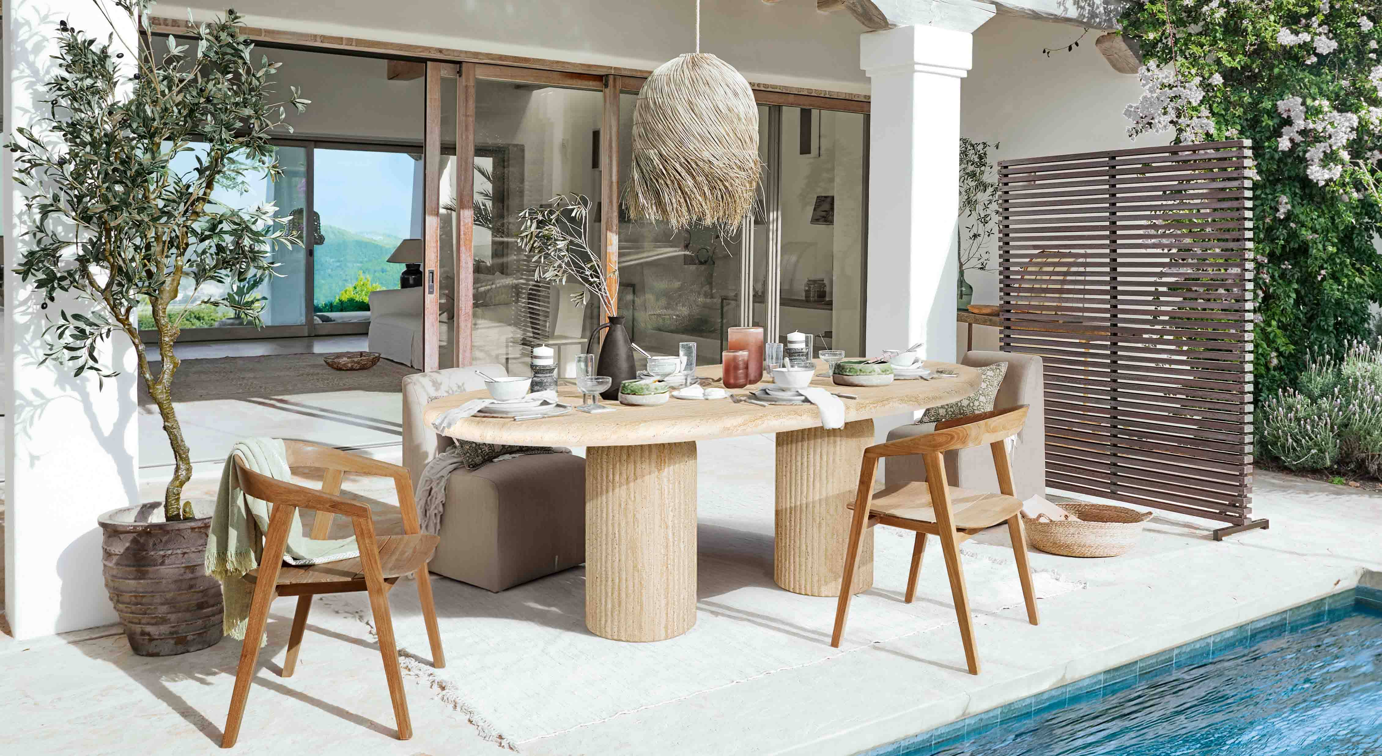 Venkovní jídelní prostor s kamenným stolem a dřevěnými židlemi u bazénu v přírodním stylu