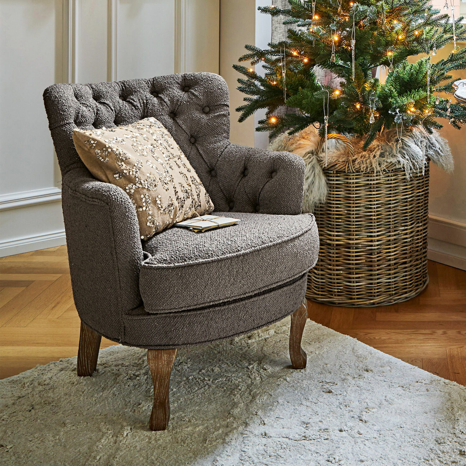 Křeslo Calgary Šedé čalouněné křeslo s dřevěnými nohami na světlém koberci vedle vánočního stromku