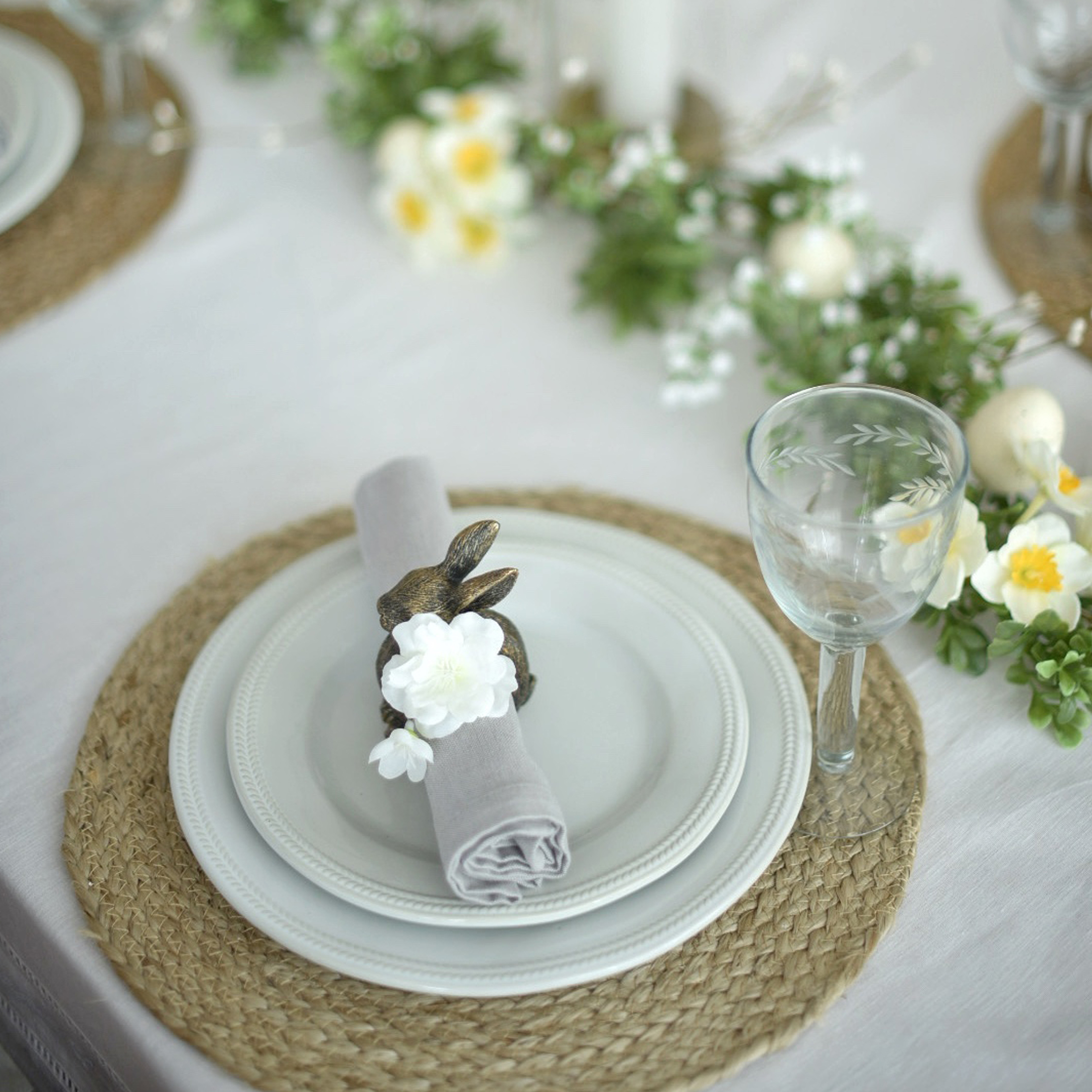 Bílé nádobí na pleteném prostírání s držákem ubrousku ve tvaru zajíce a květinovou výzdobou