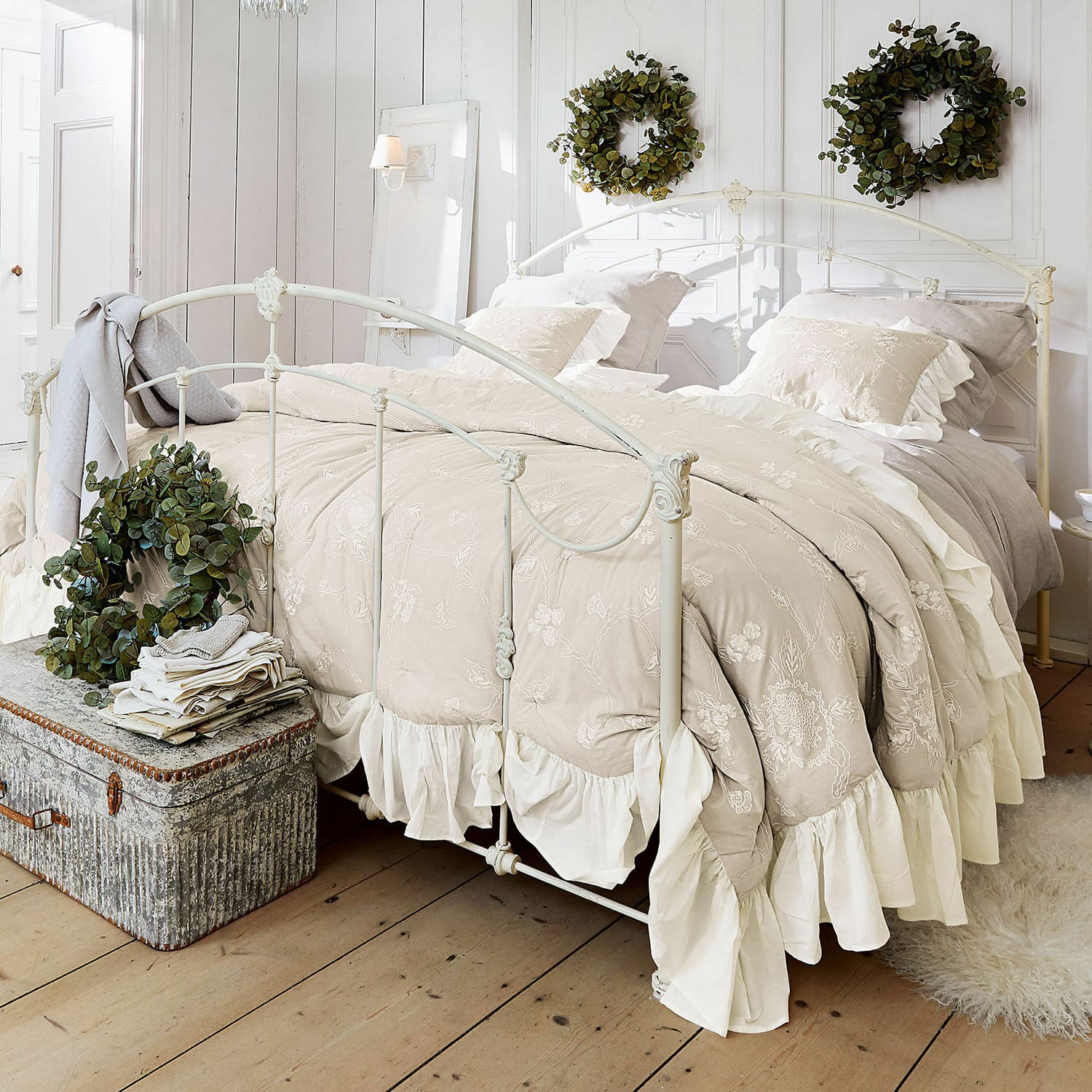 Přehoz Clarissa Béžové vyšívané povlečení s volánky na kovové posteli v světlé ložnici se zelenými věnci