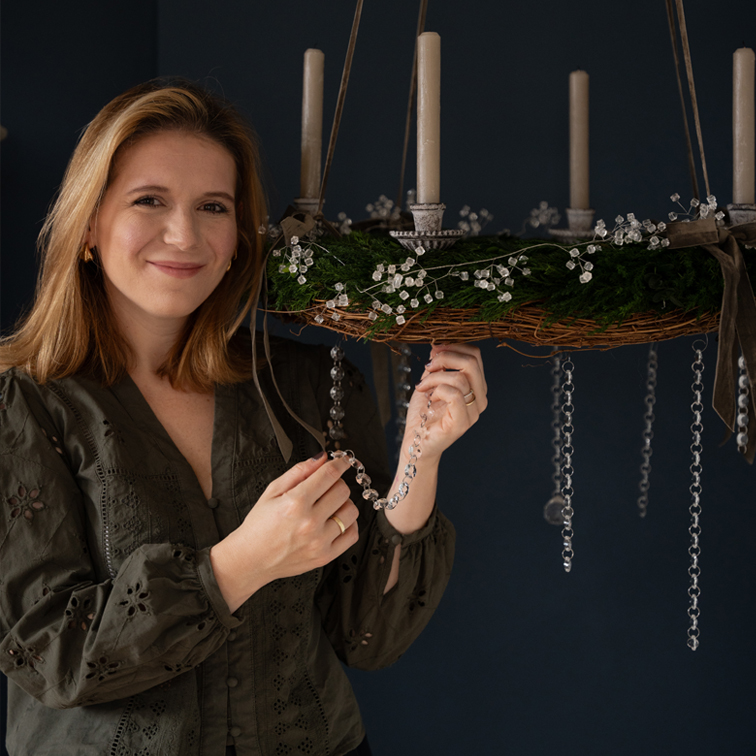 Žena zdobí zelený adventní věnec s bílými svíčkami a průhlednými ozdobami na řetězech