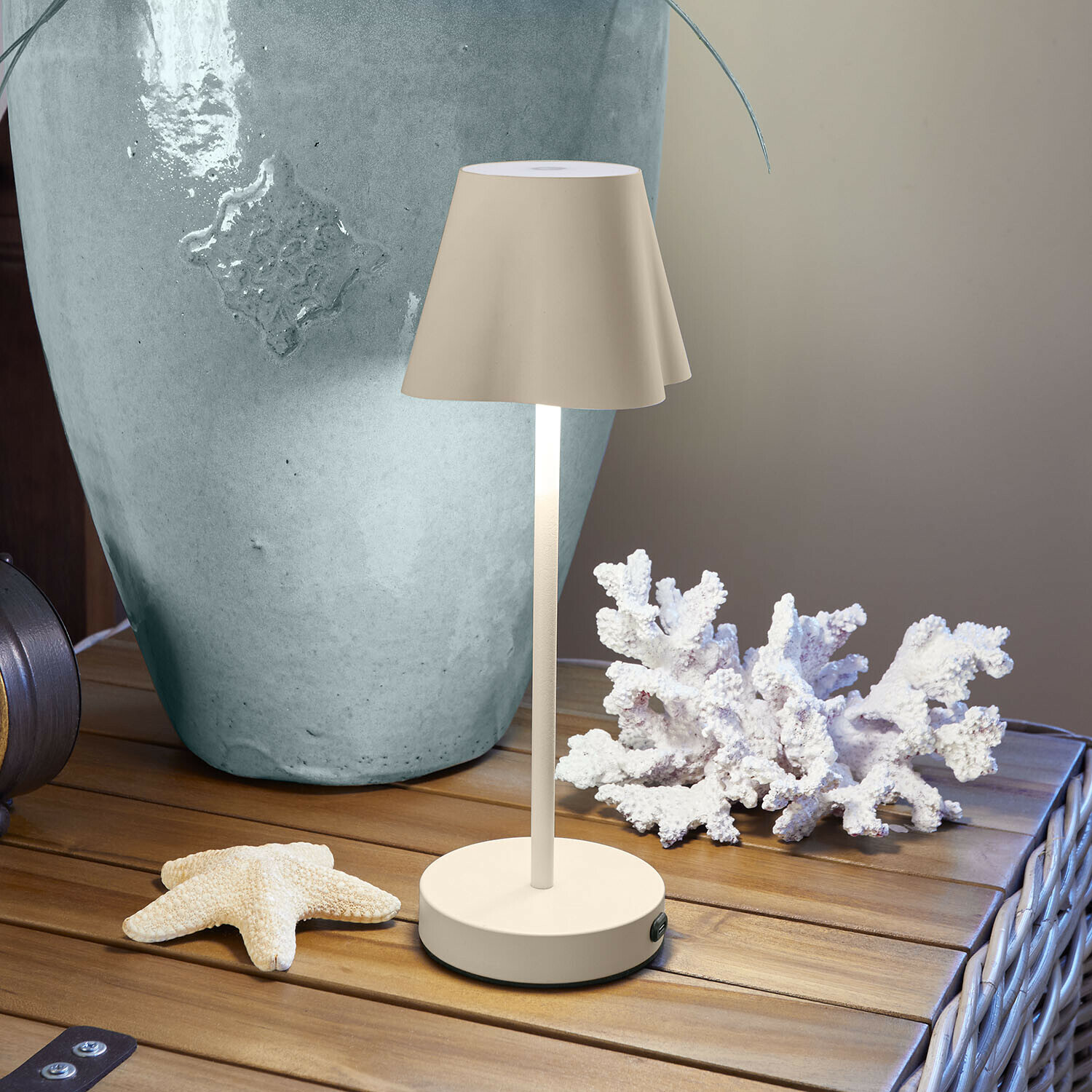 Dobíjecí stolní lampa Tenari Béžová kovová stolní lampa na dřevěném stole s mořskou dekorací a velkou vázu