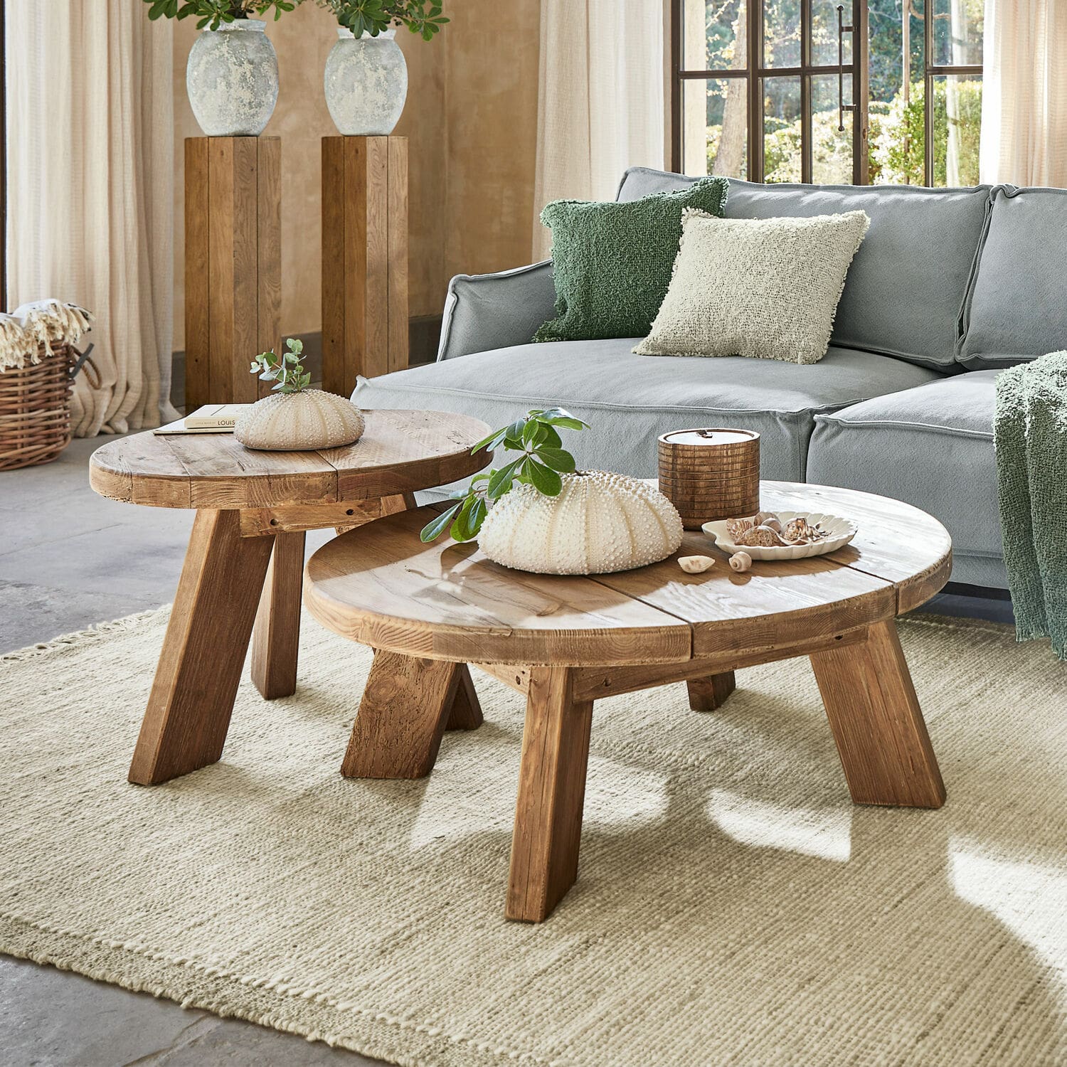 Konferenční stolky, 2dílná sada Oteley Dva kulaté dřevěné konferenční stolky v přírodní barvě na světlém koberci v obývacím pokoji se šedou pohovkou
