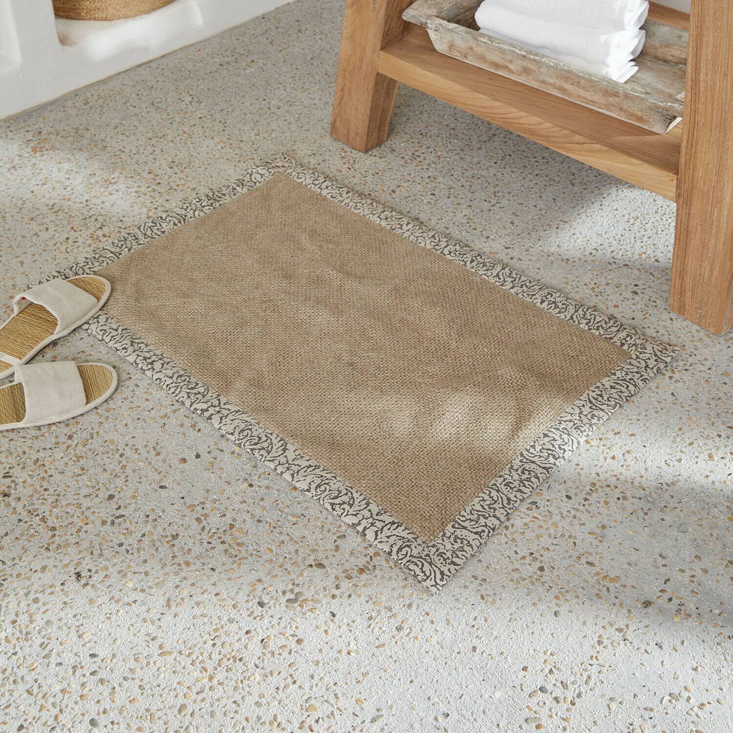 Béžový koberec z přírodního materiálu s šedým ozdobným lemem na světlé kamenné podlaze