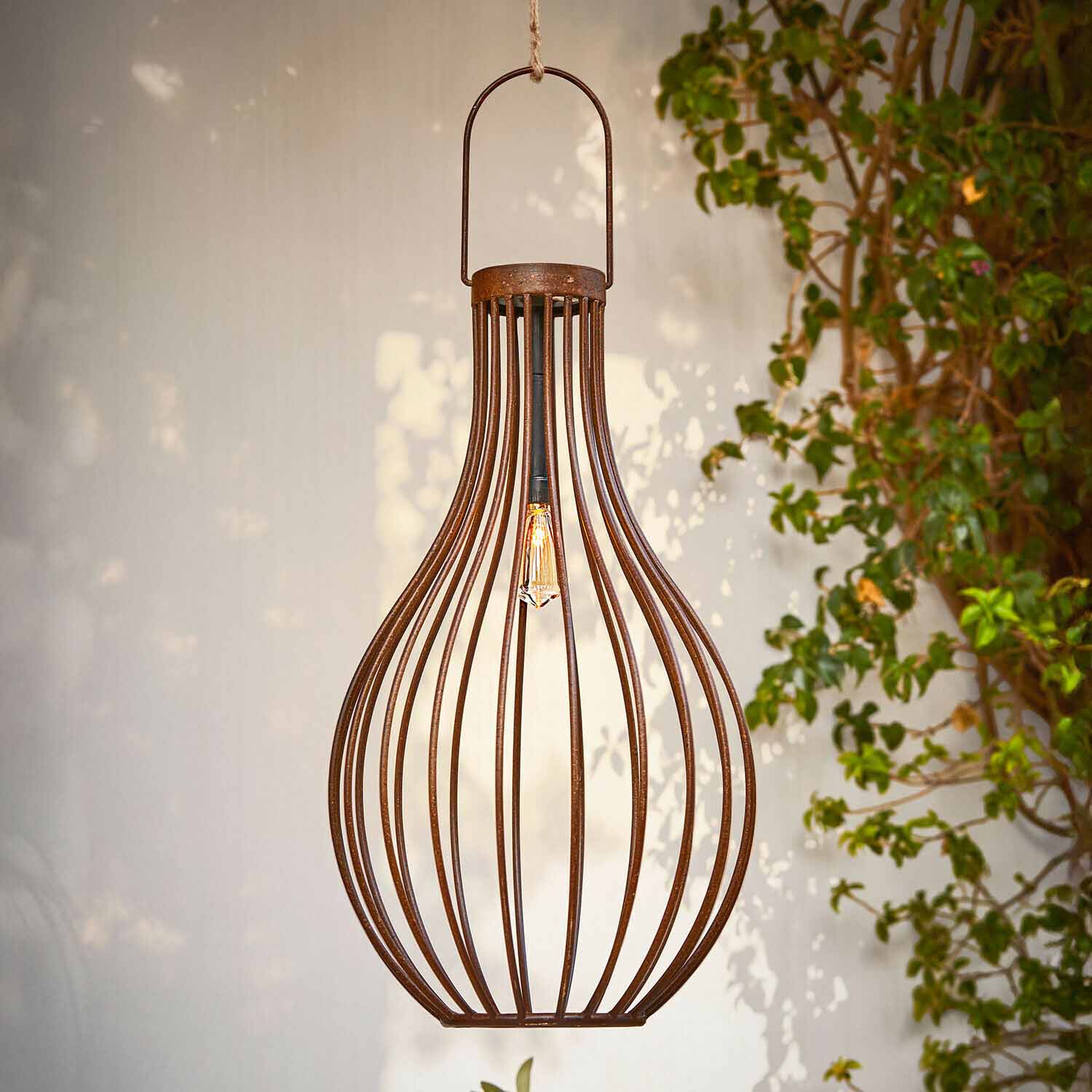 Závěsná kovová lampa ve tvaru hrušky s rezavým povrchem a viditelnou žárovkou, zahradní dekorace
