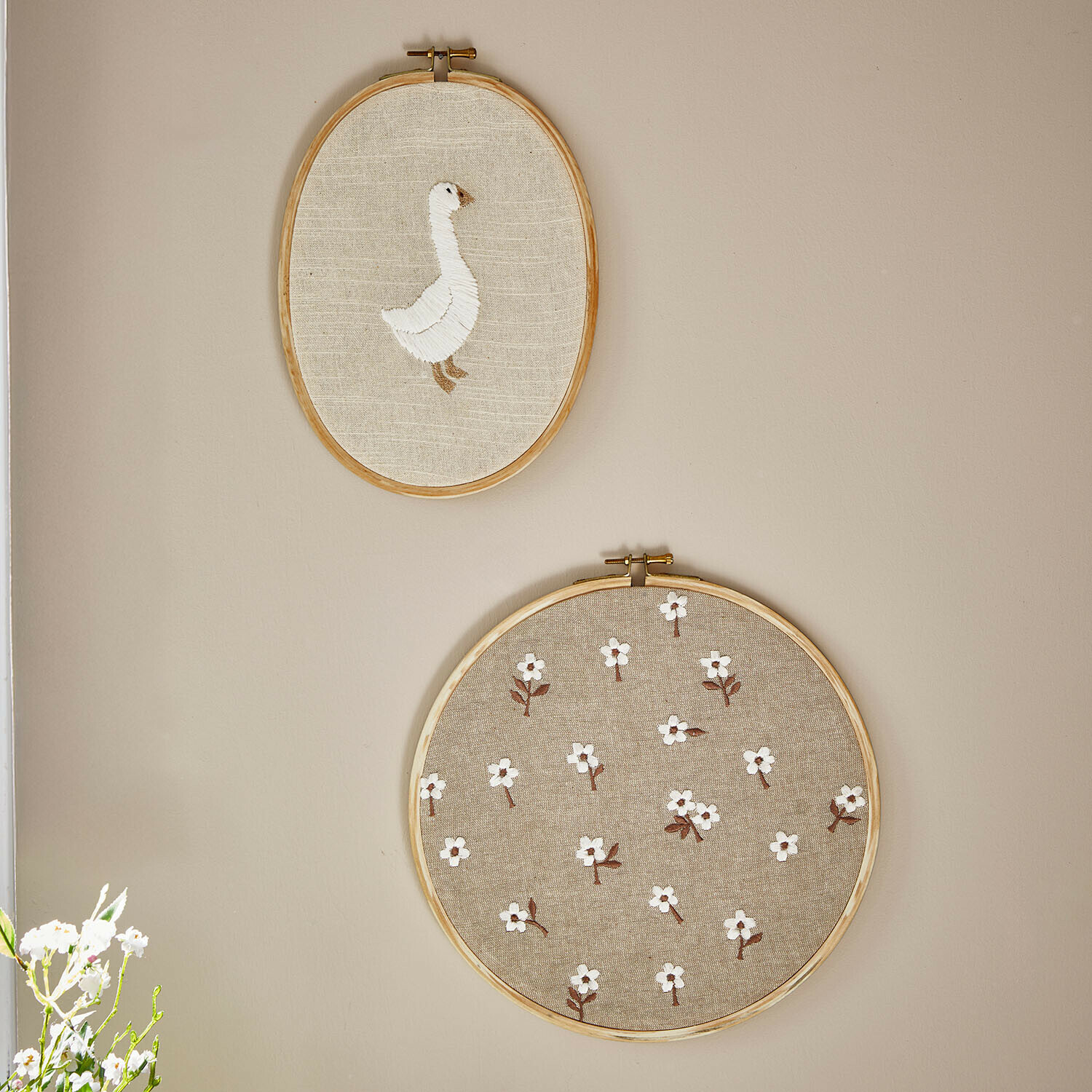 Dva vyšívané rámečky z přírodního lnu s bílou husou a květinovým vzorem na stěně