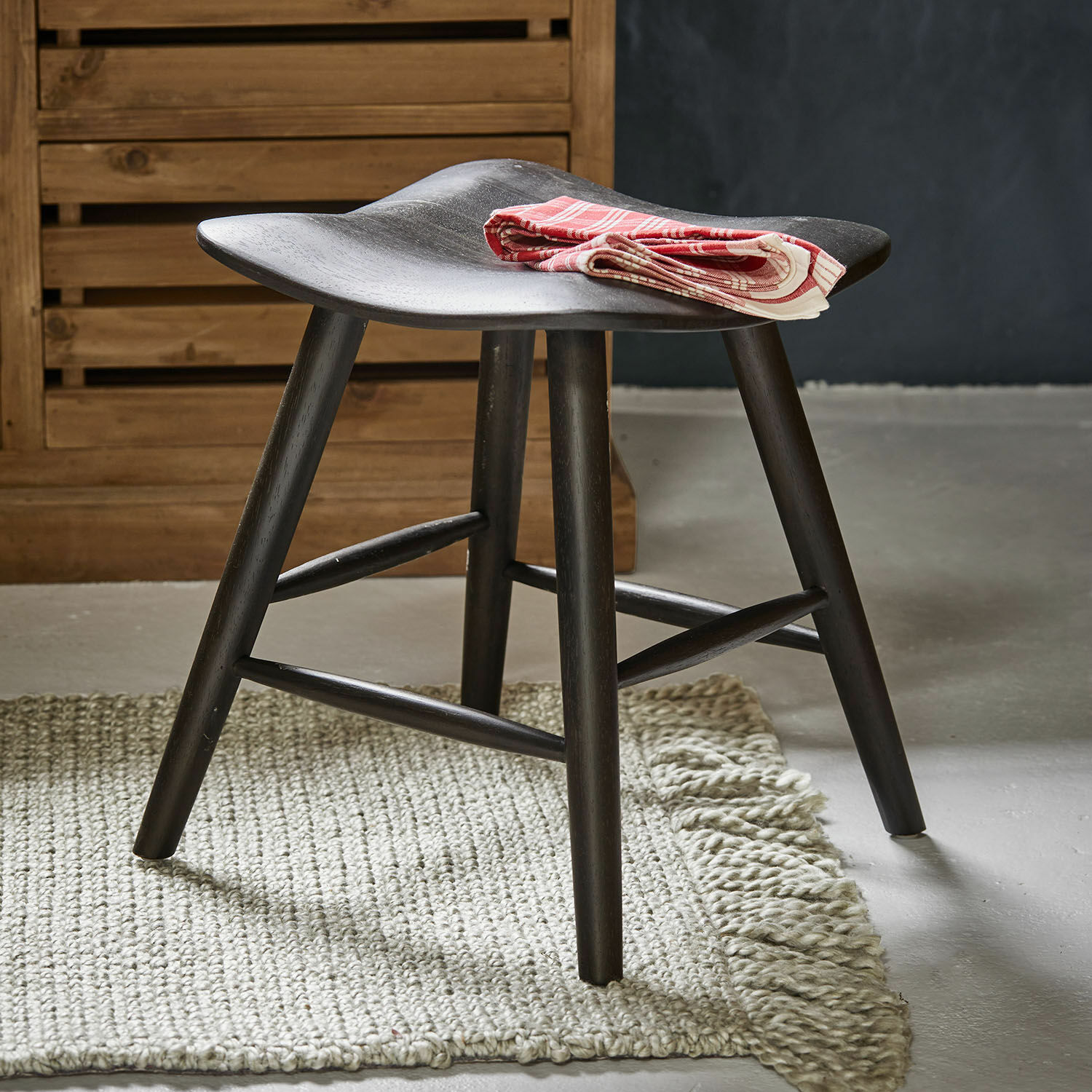 Černá dřevěná stolička s prohnutým sedákem na světlém koberci, červený dekorativní ubrousek