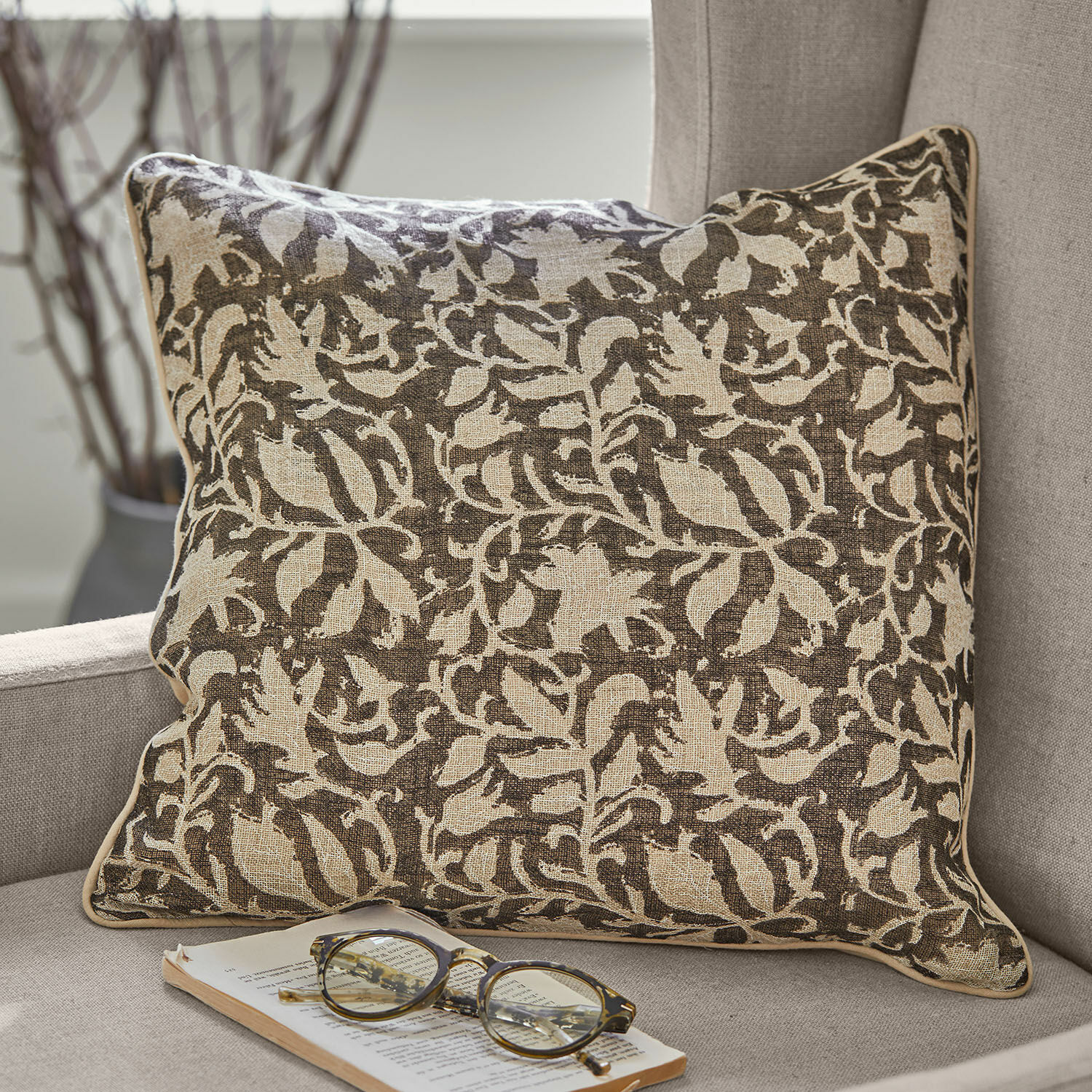 Povlaky na polštářky, 2dílná sada Ziradayn Hnědo-béžový bavlněný dekorativní polštář s rostlinným vzorem na šedé pohovce s brýlemi a knihou