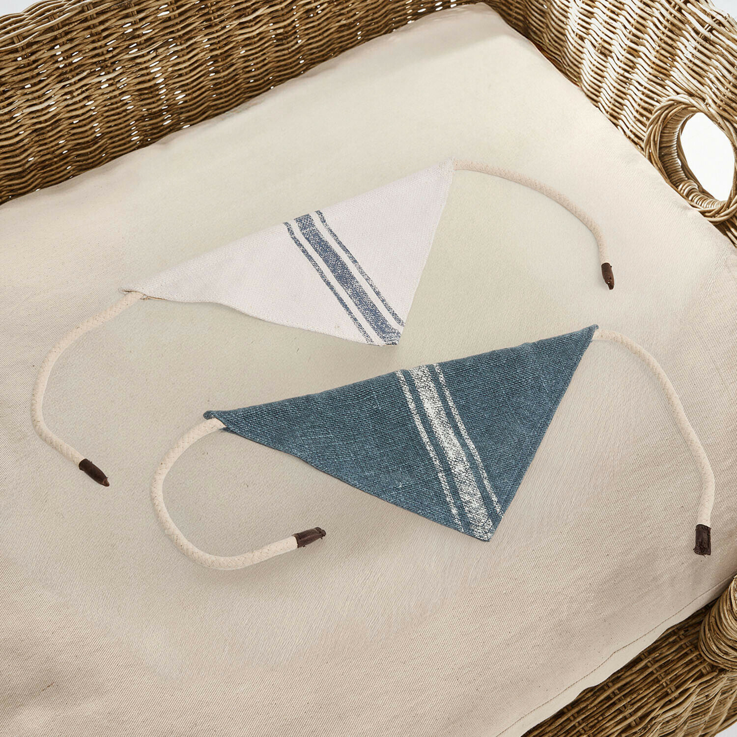 Dva trojúhelníkové bavlněné chrániče ramen v bílé a modré barvě s pruhy na proutěném křesle