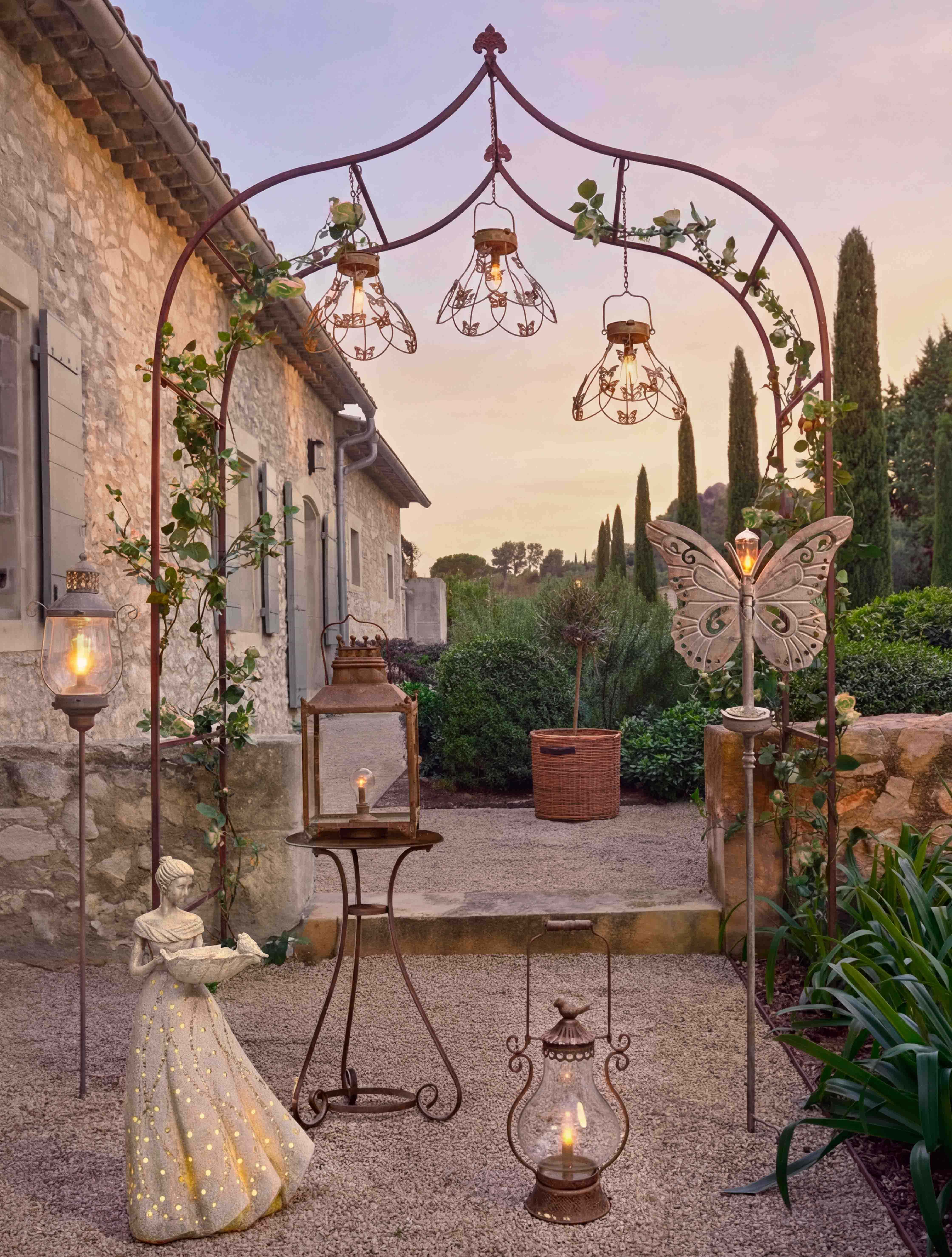 Dekorativní kovový oblouk s lucernami a sochou ženy v zahradě osvětlený teplým světlem