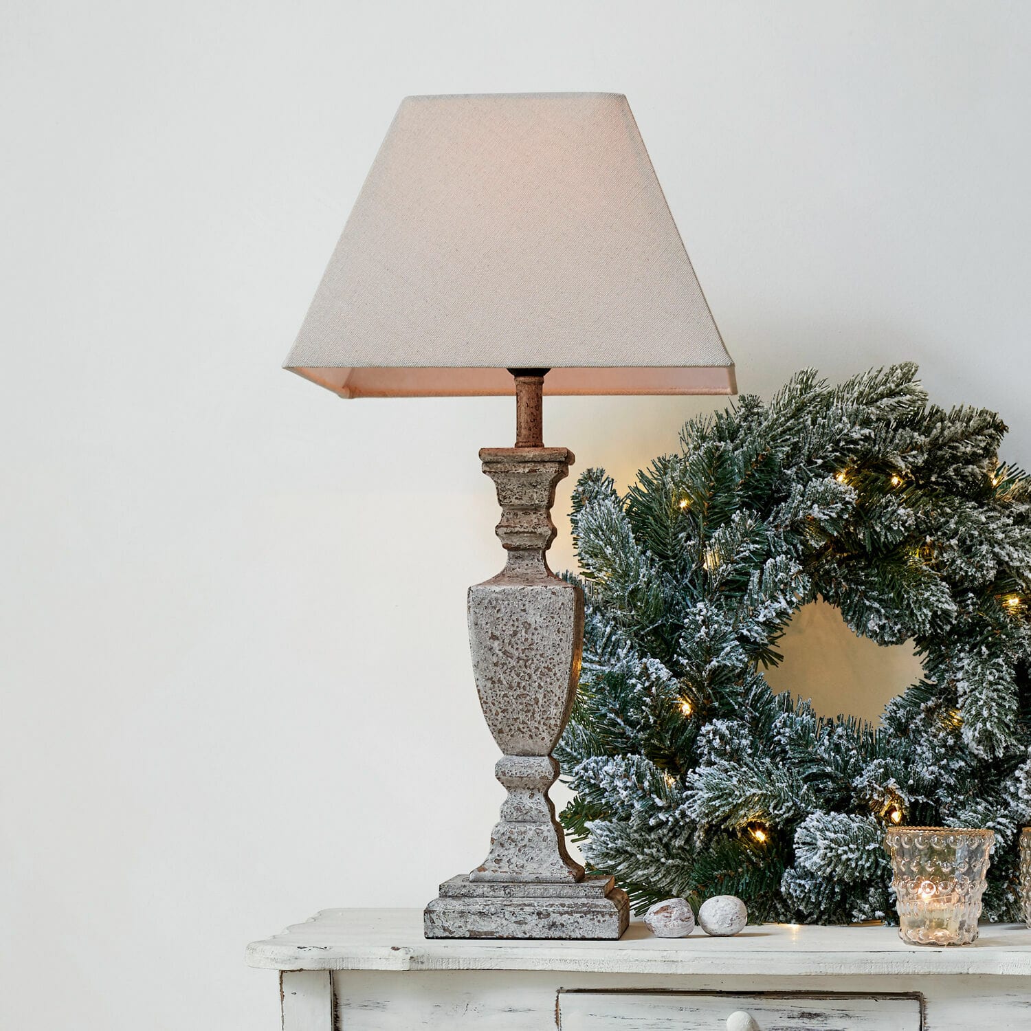 Stolní lampa Gorham Stolní lampa z kamene v béžové barvě s textilním stínidlem vedle vánočního věnce se zelenými větvemi a světýlky