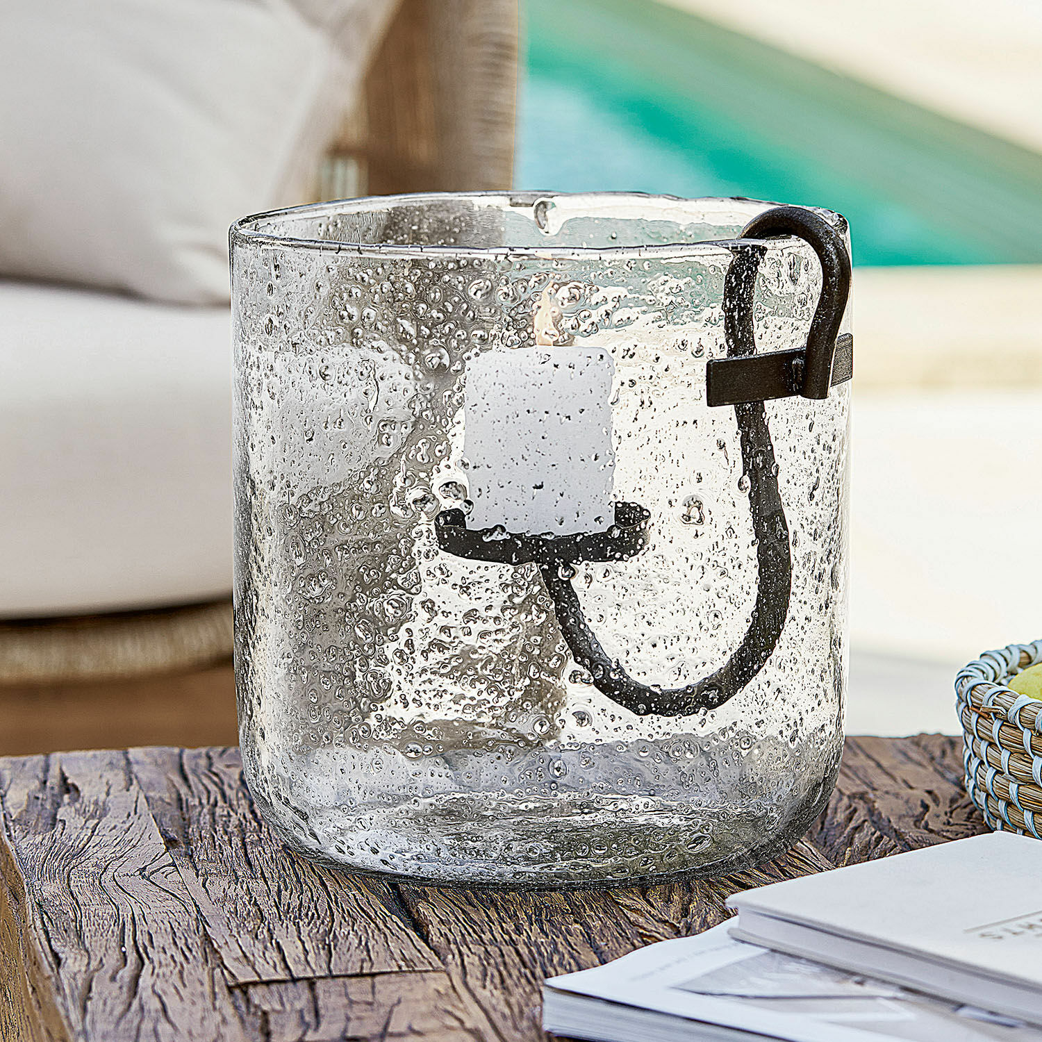 Skleněný svícen s bublinkami a černým kovovým držadlem na dřevěném stole