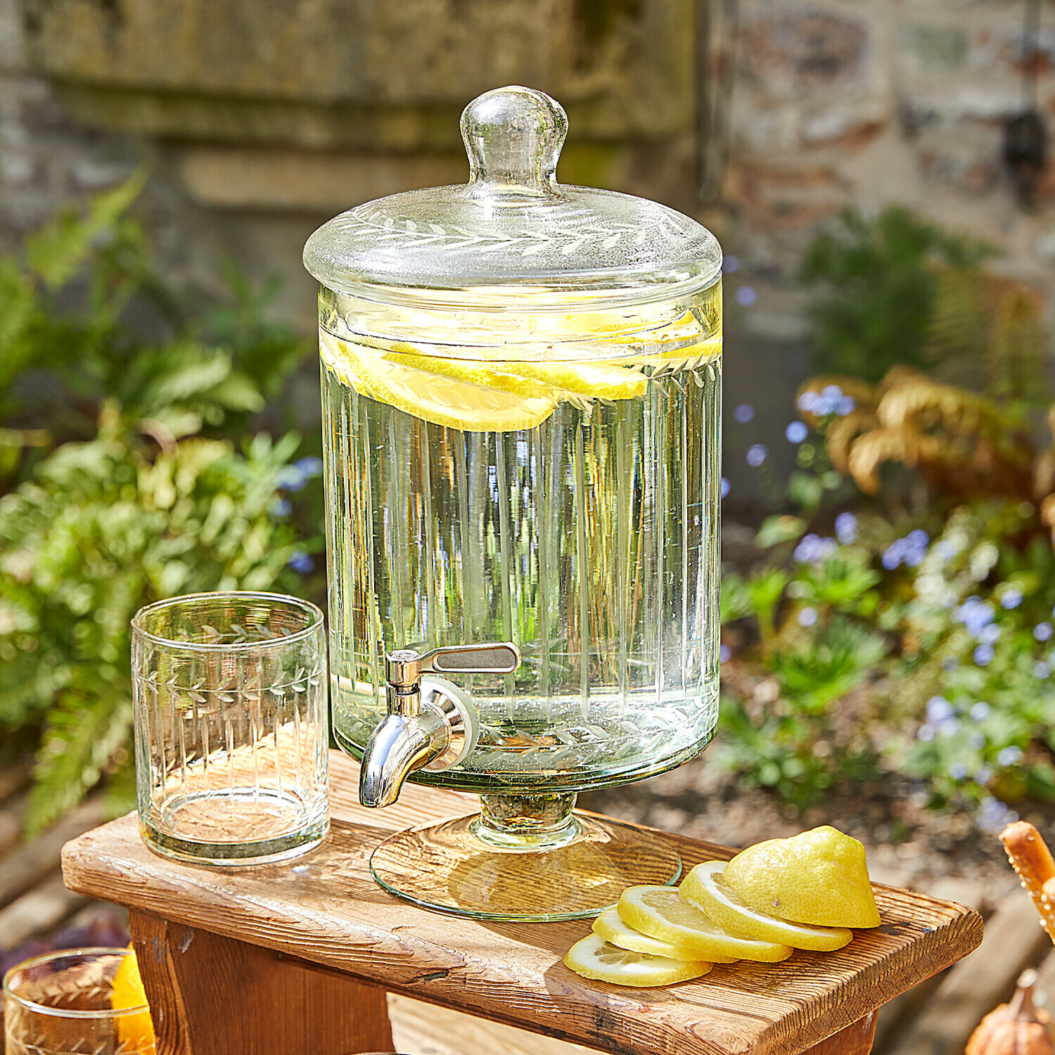 Nádoba na nápoje Makiya Skleněný nápojový dávkovač s víkem a kohoutkem, plátky citronu, na dřevěném stole venku