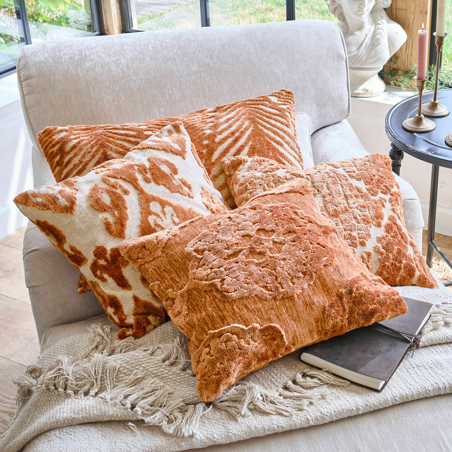 Sada oranžových dekorativních polštářů s vzory na světlé pohovce s přehozem