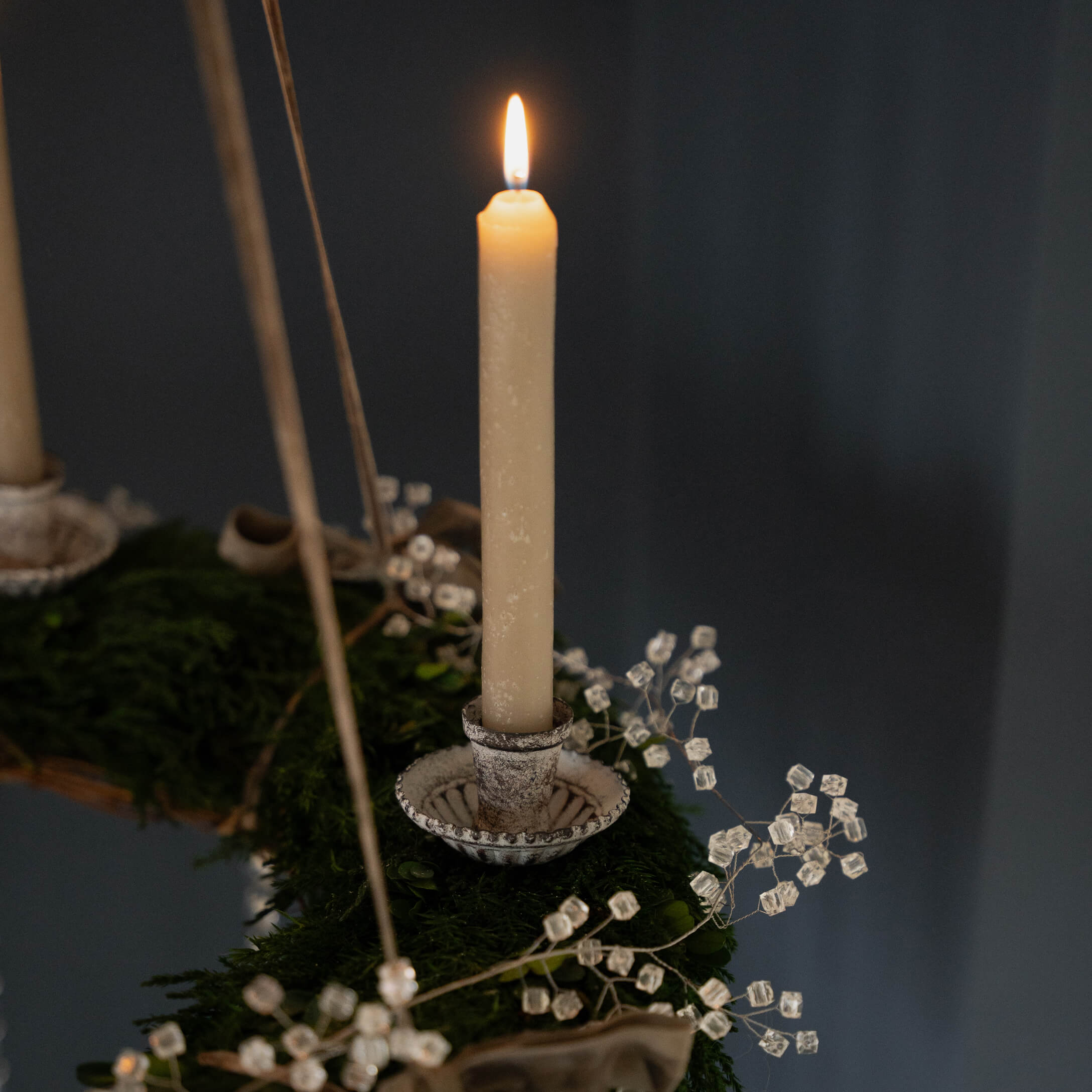 Béžová svíčka na kovovém svícnu na zeleném adventním věnci s krystalovou dekorací