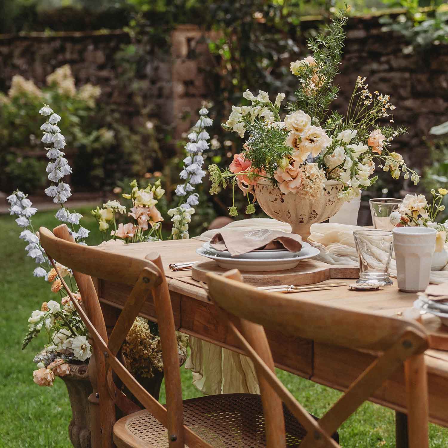 Dřevěný zahradní stůl s rustikálními židlemi a květinovou dekorací v pastelových barvách