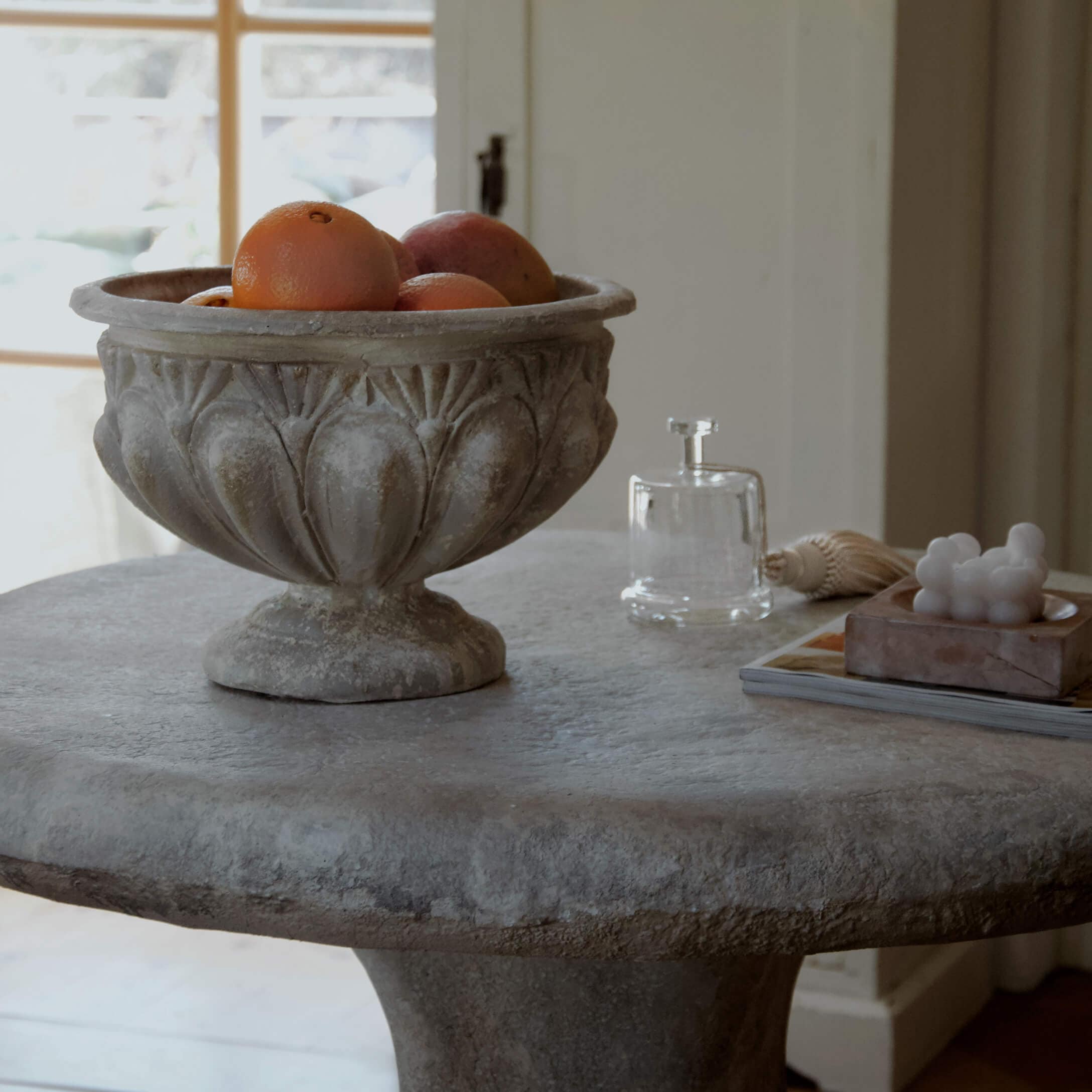 Dekorativní kamenná mísa s pomeranči na kamenném stole v světlém interiéru