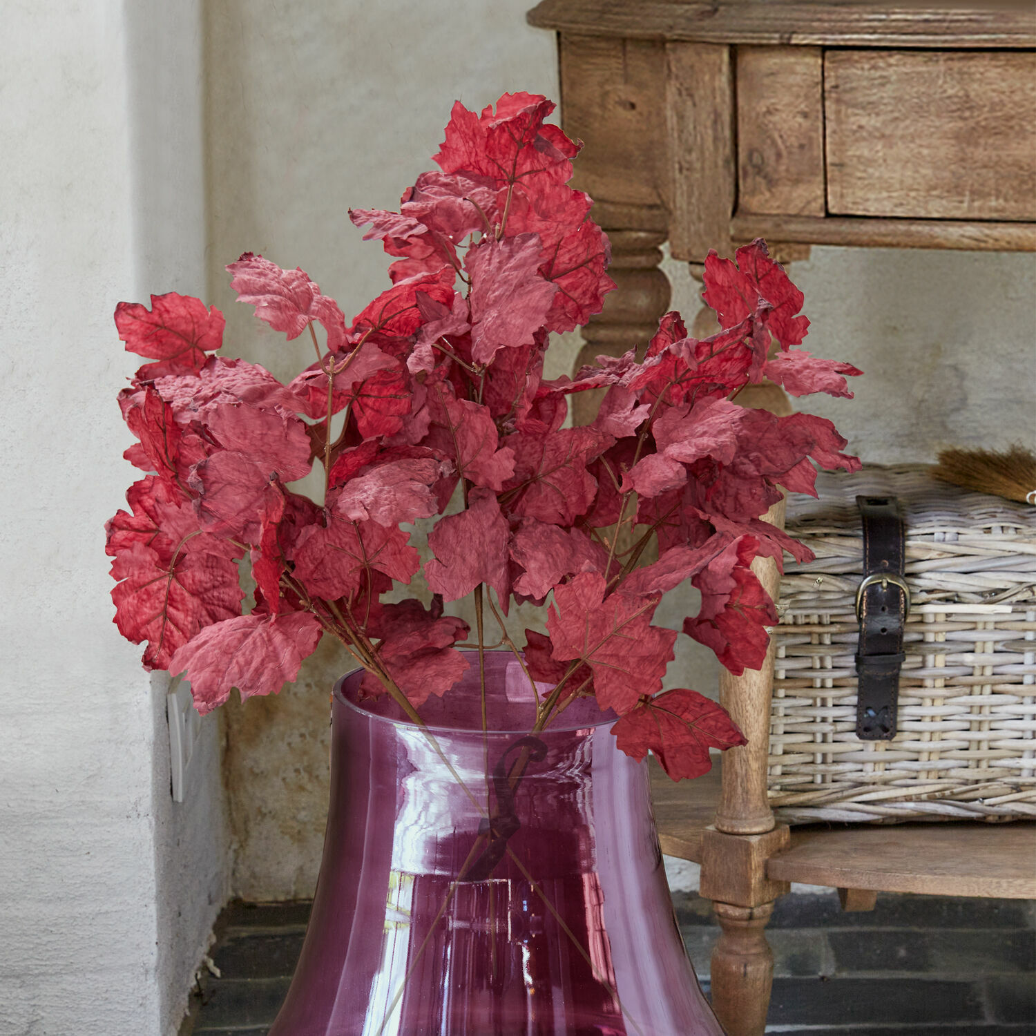 Dekorační větvičky, 3dílná sada Camirissa Dekorativní červené listy ve fialové průhledné skleněné váze před dřevěným nábytkem