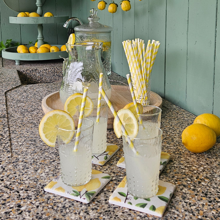 Sklenice s limonádou a plátky citronu na kamenném pultu s papírovými brčky a tácem s citrony