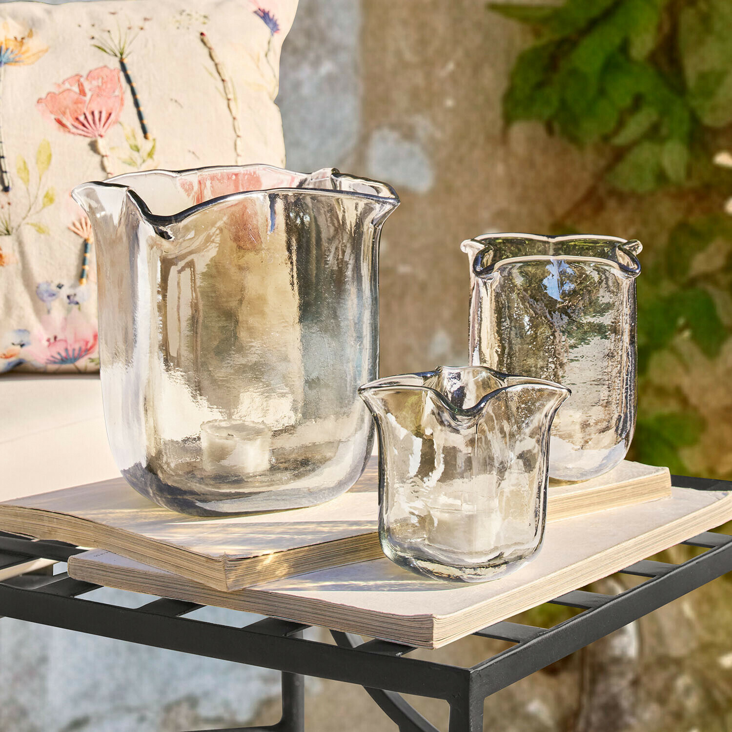 Sada tří průhledných skleněných svícnů nepravidelného tvaru na knihách