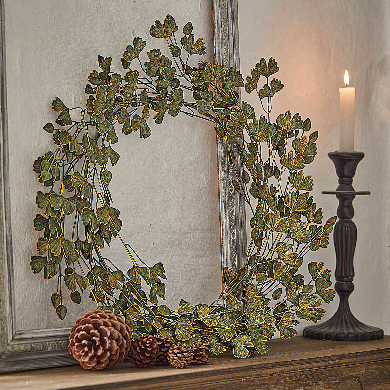Dekorativní věnec ze zelených listů na dřevěné polici se šiškami a svíčkou