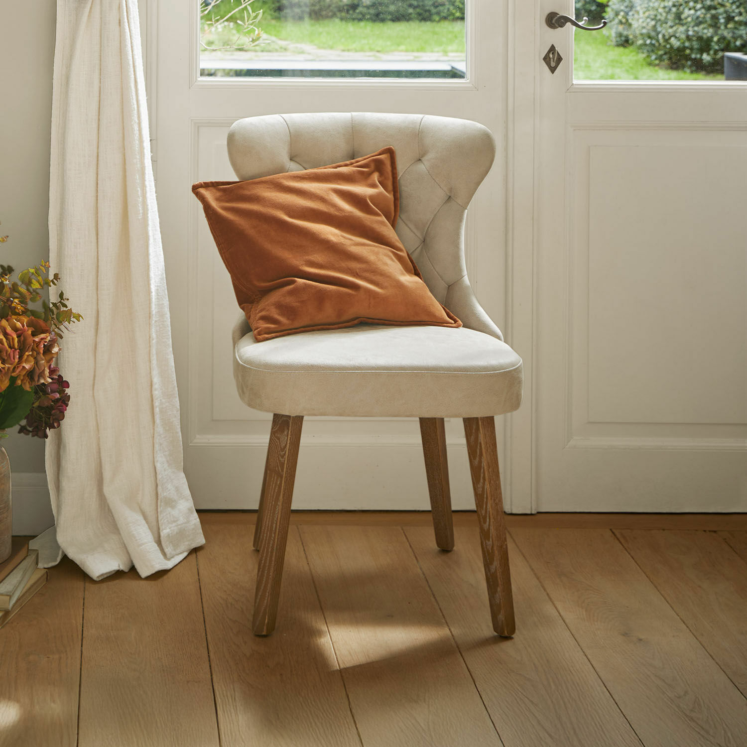 Béžová čalouněná židle s dřevěnými nohami a oranžovým polštářem v světlém interiéru