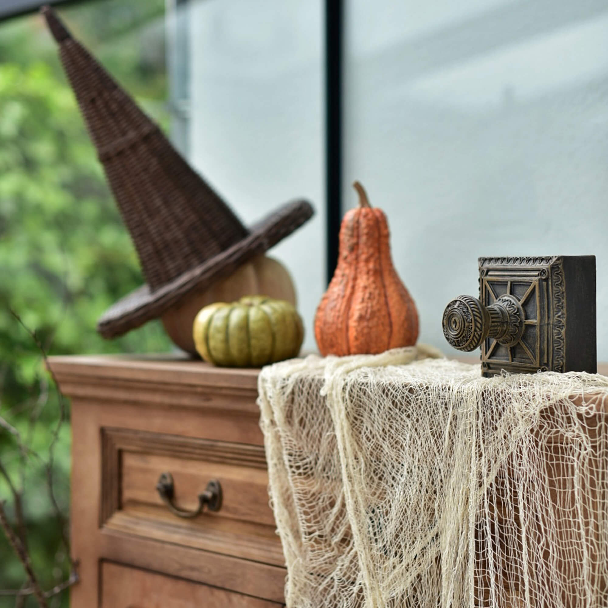 Dřevěná komoda s proutěným čarodějnickým kloboukem a dýněmi na Halloween