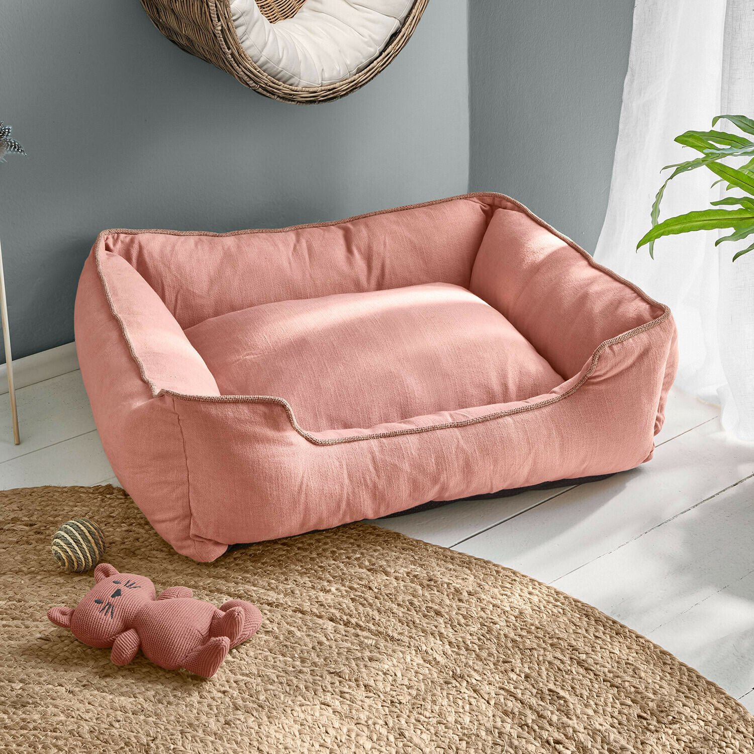 Růžový pelíšek pro psa z měkkého materiálu na světlé podlaze s hračkou kočky a jutovým kobercem