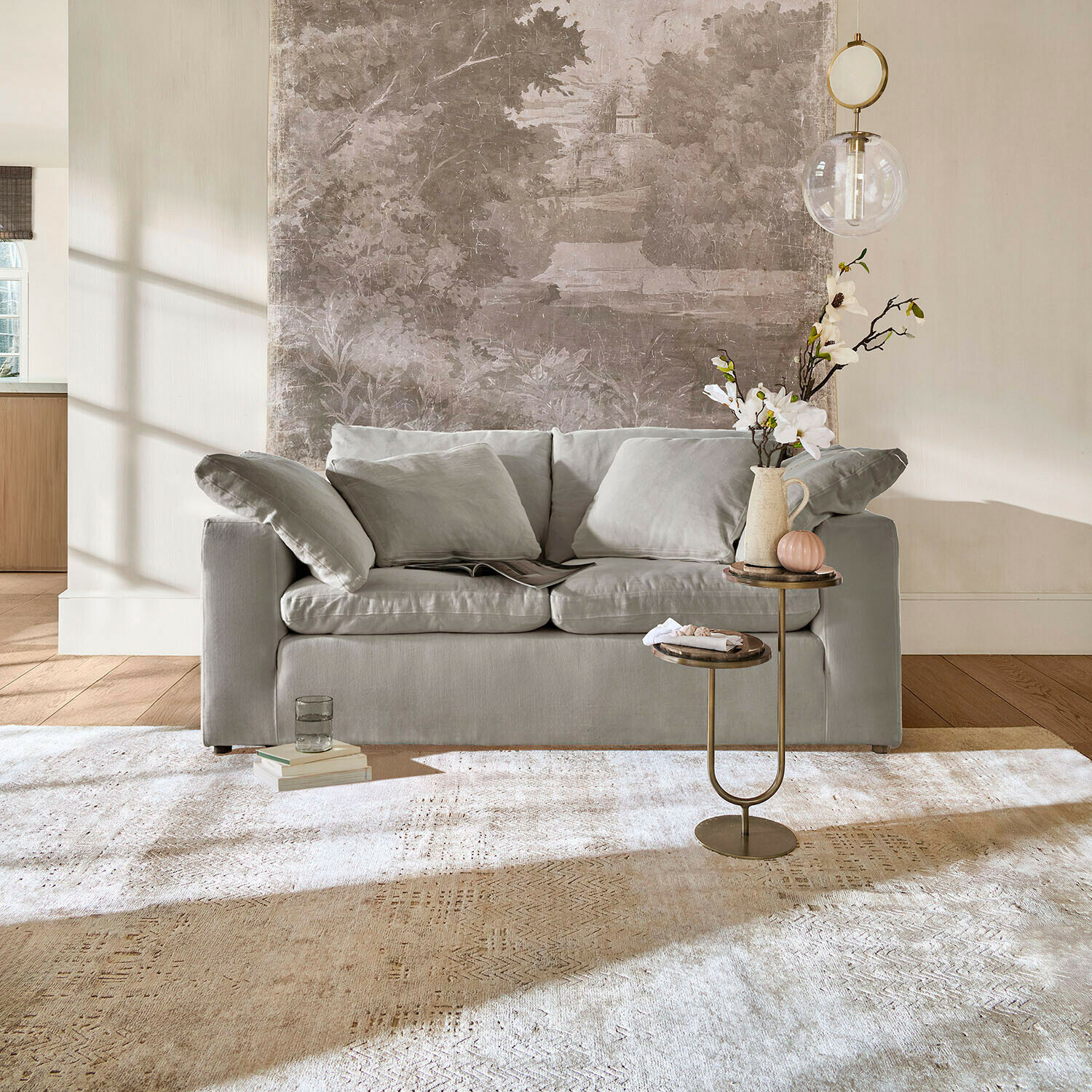 Šedá pohovka s měkkými polštáři v světlém obývacím pokoji s dekorativním stolkem a kobercem