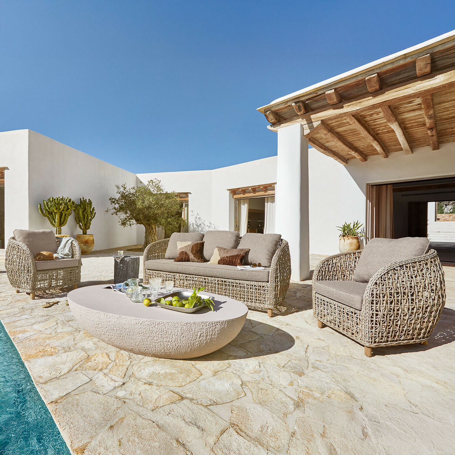 Sada zahradního nábytku z béžového ratanu s polštáři na kamenné terase u bazénu za slunečného dne