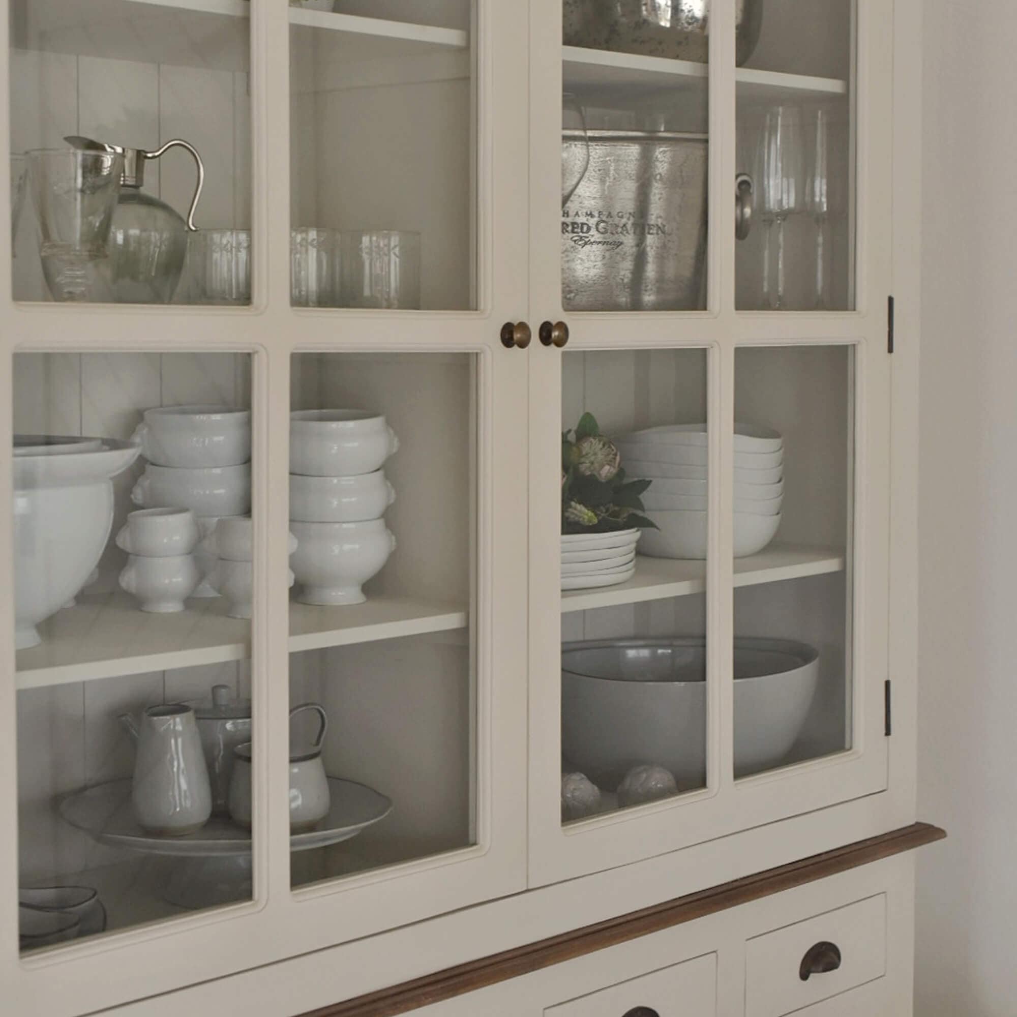Krémová dřevěná vitrína se skleněnými dveřmi a bílým porcelánem uvnitř, jídelní nábytek