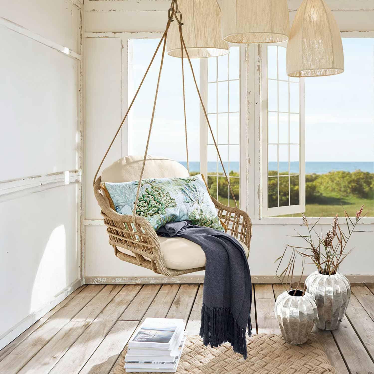 Závěsné křeslo z přírodního pleteného lana s krémovým polštářem a tmavě modrou dekou v světlé místnosti