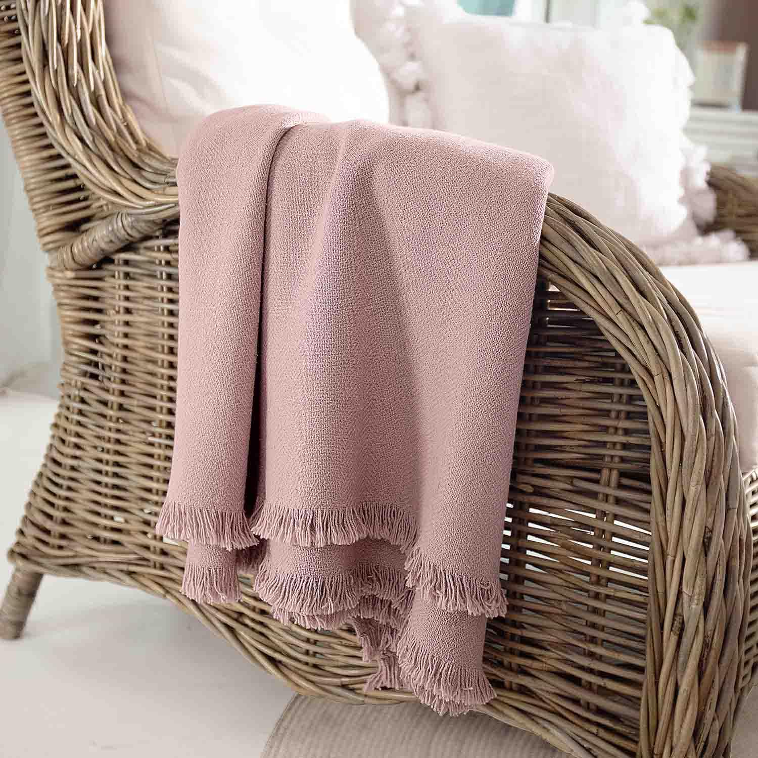 Růžová deka z měkkého materiálu s třásněmi na proutěném křesle, dekorace a pohodlí