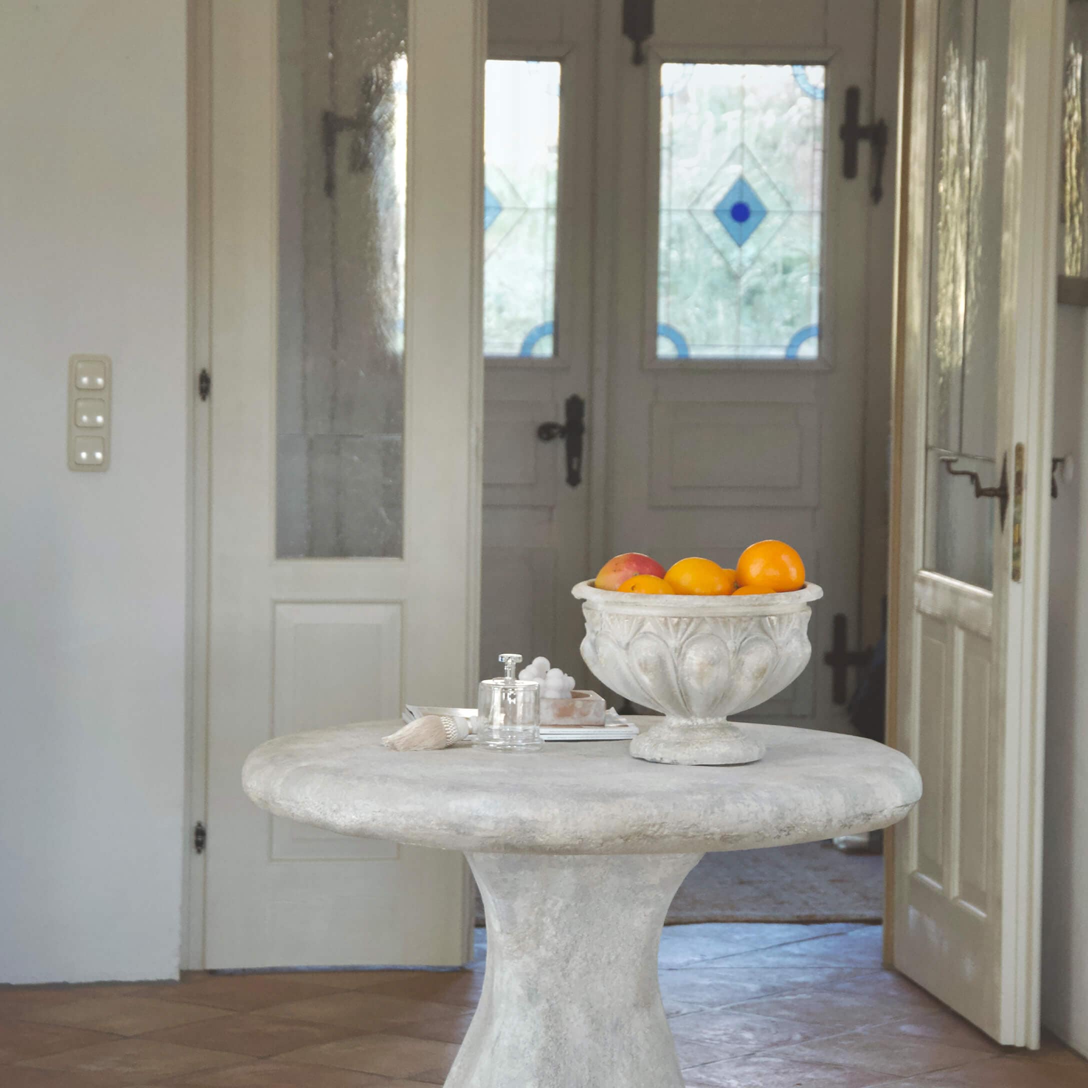 Kulatý stůl z světlého betonu s dekorativní vintage miskou plnou pomerančů