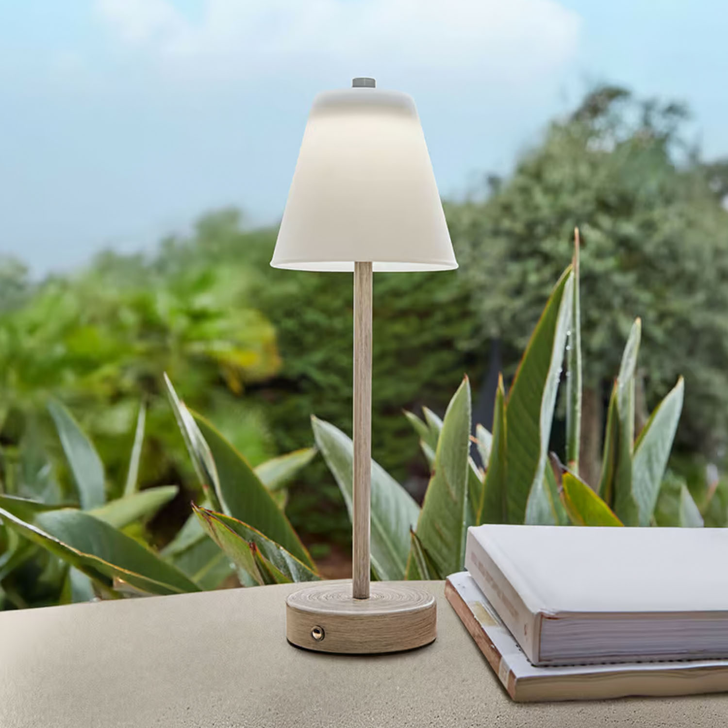 Stolní lampa z světlého dřeva s bílým stínidlem před zelenými rostlinami, interiérová dekorace