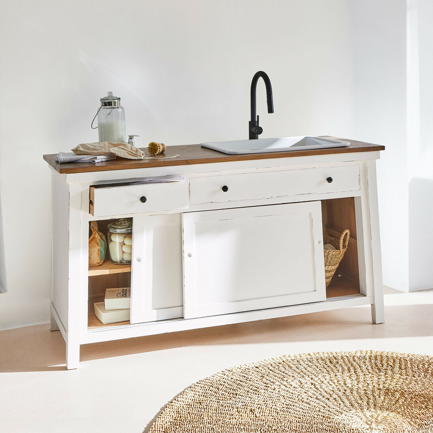 Bílá dřevěná skříňka s tmavým dřevěným povrchem, bílým dřezem a černou baterií, otevřené zásuvky