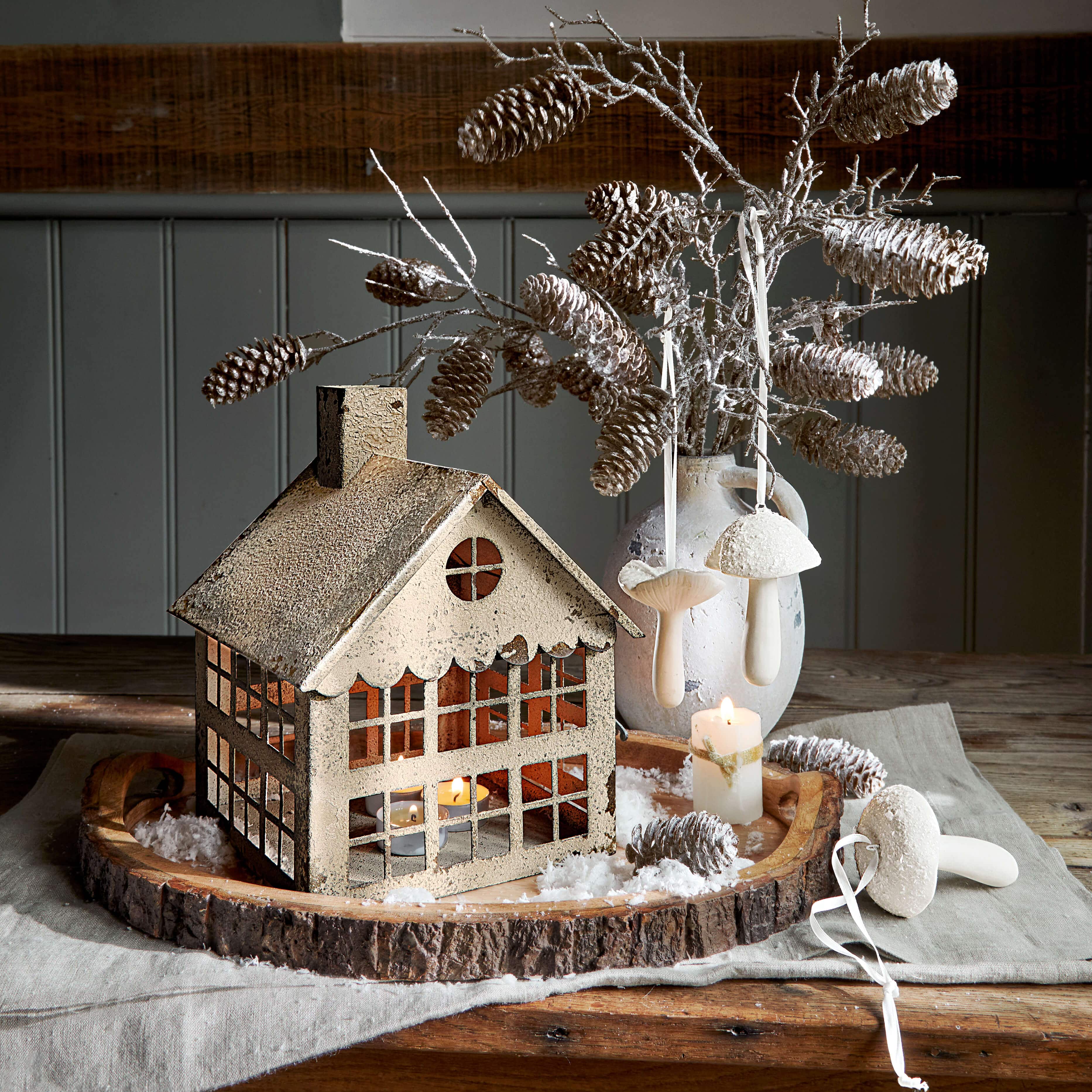 Dekorativní kovový domeček s čajovou svíčkou na dřevěném podnosu se šiškami a bílými houbami