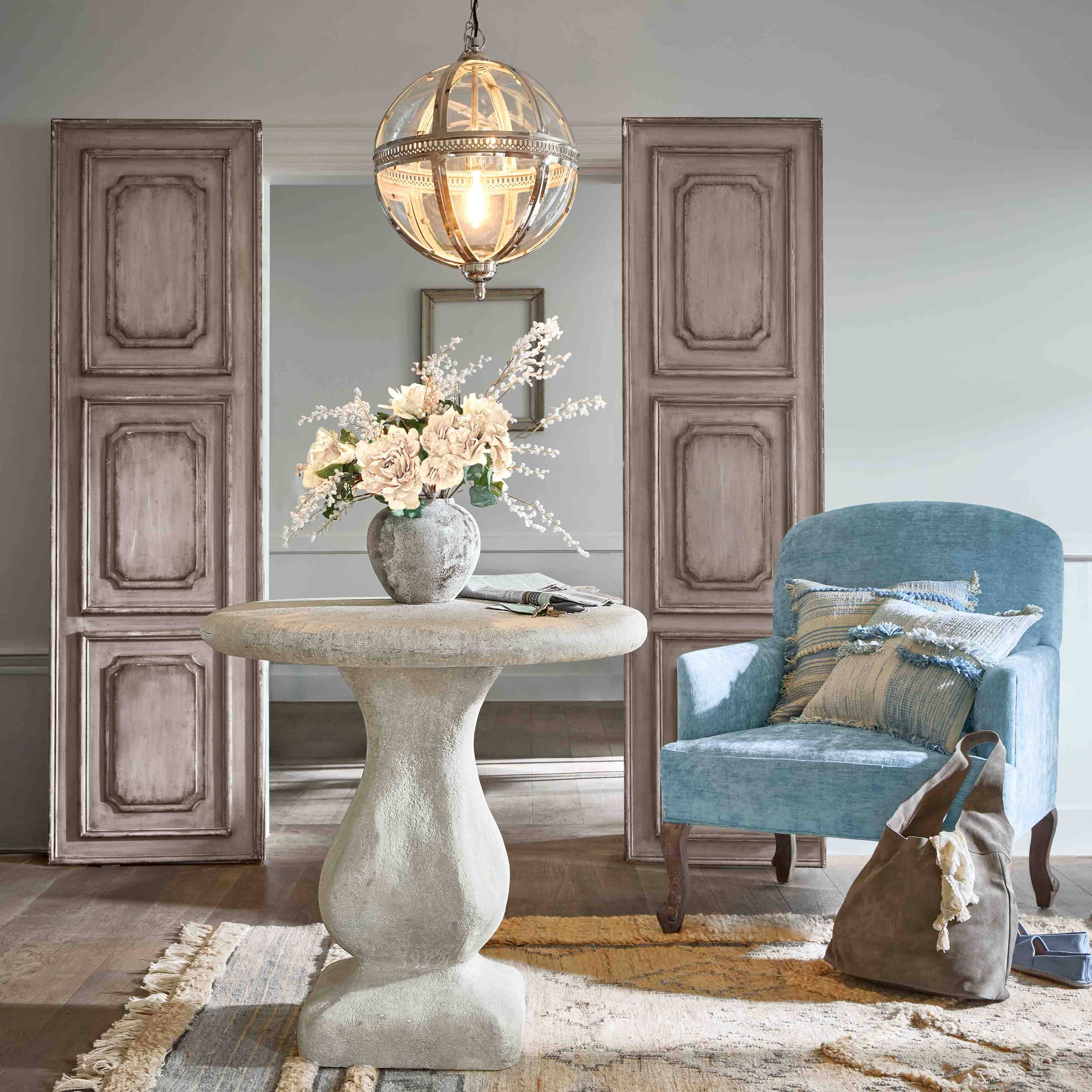 Kulatý betonový stůl s váza květin a modré křeslo s polštáři v elegantním obývacím pokoji