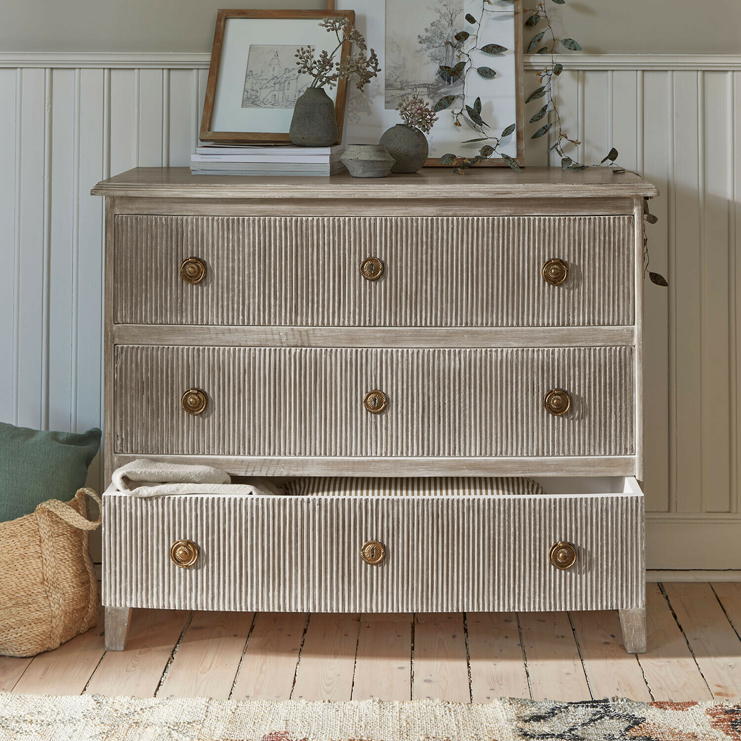 Komoda z žebrovaného dřeva v béžové barvě s mosaznými úchyty a dekoracemi na vrchu