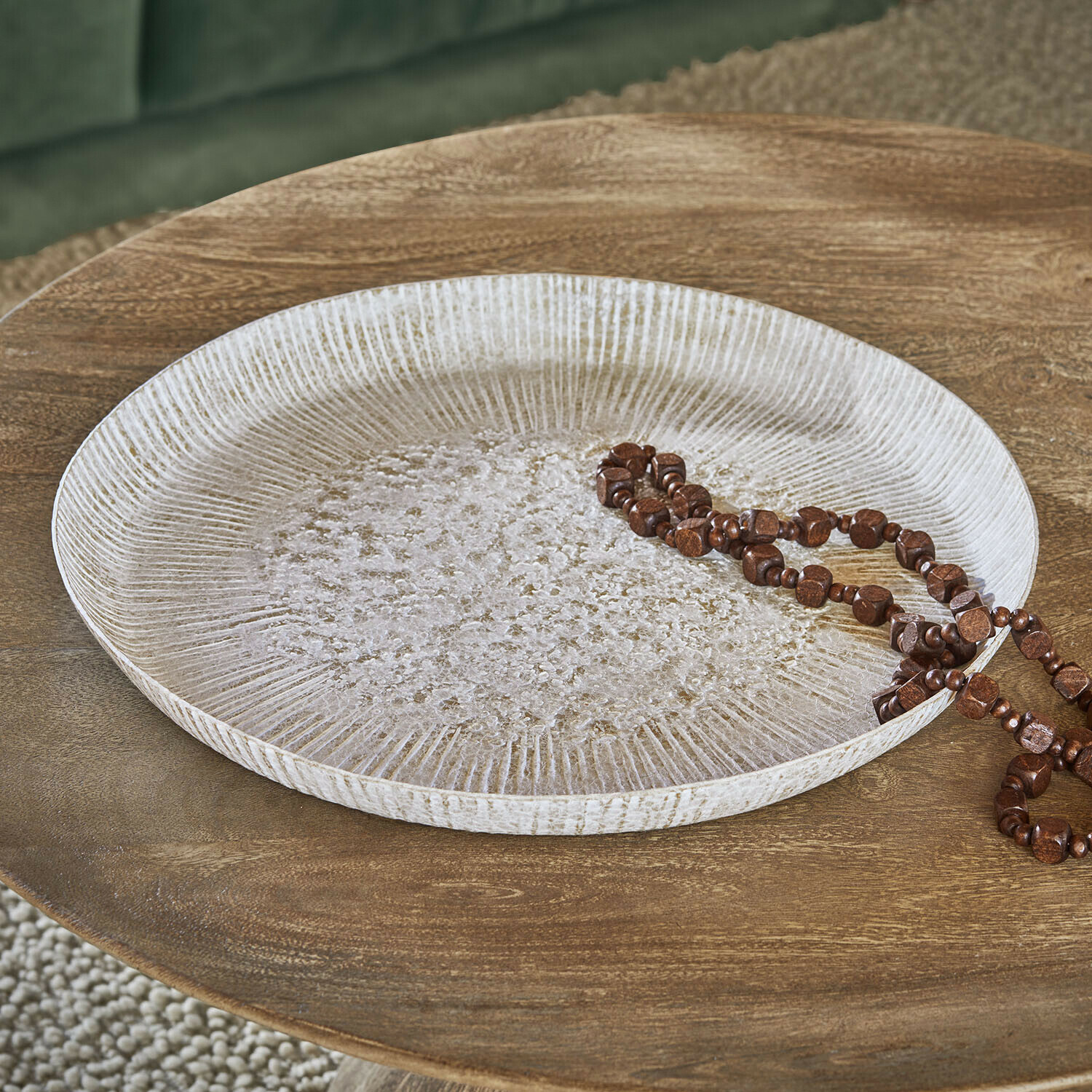 Podnos Gravière Kulatý dekorativní tác z bílého dřeva s texturou na dřevěném stole s hnědým náhrdelníkem