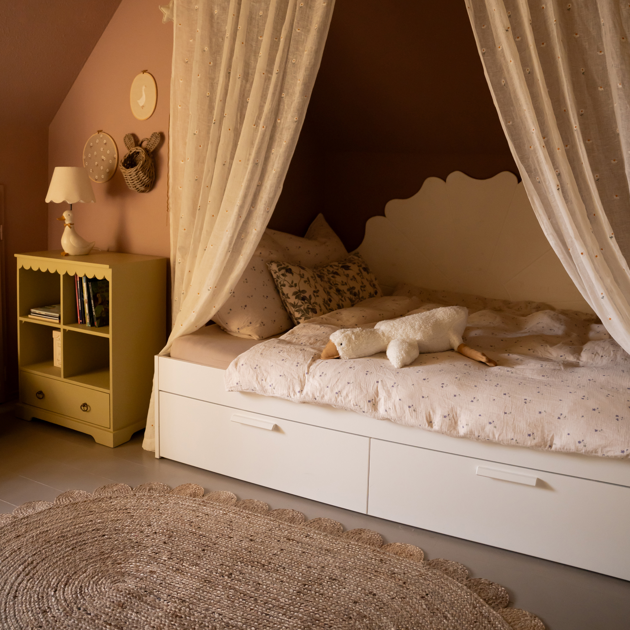 Pohodlná dětská postel s bílým rámem, záclonami a plyšovou hračkou husy na vzorovaném povlečení