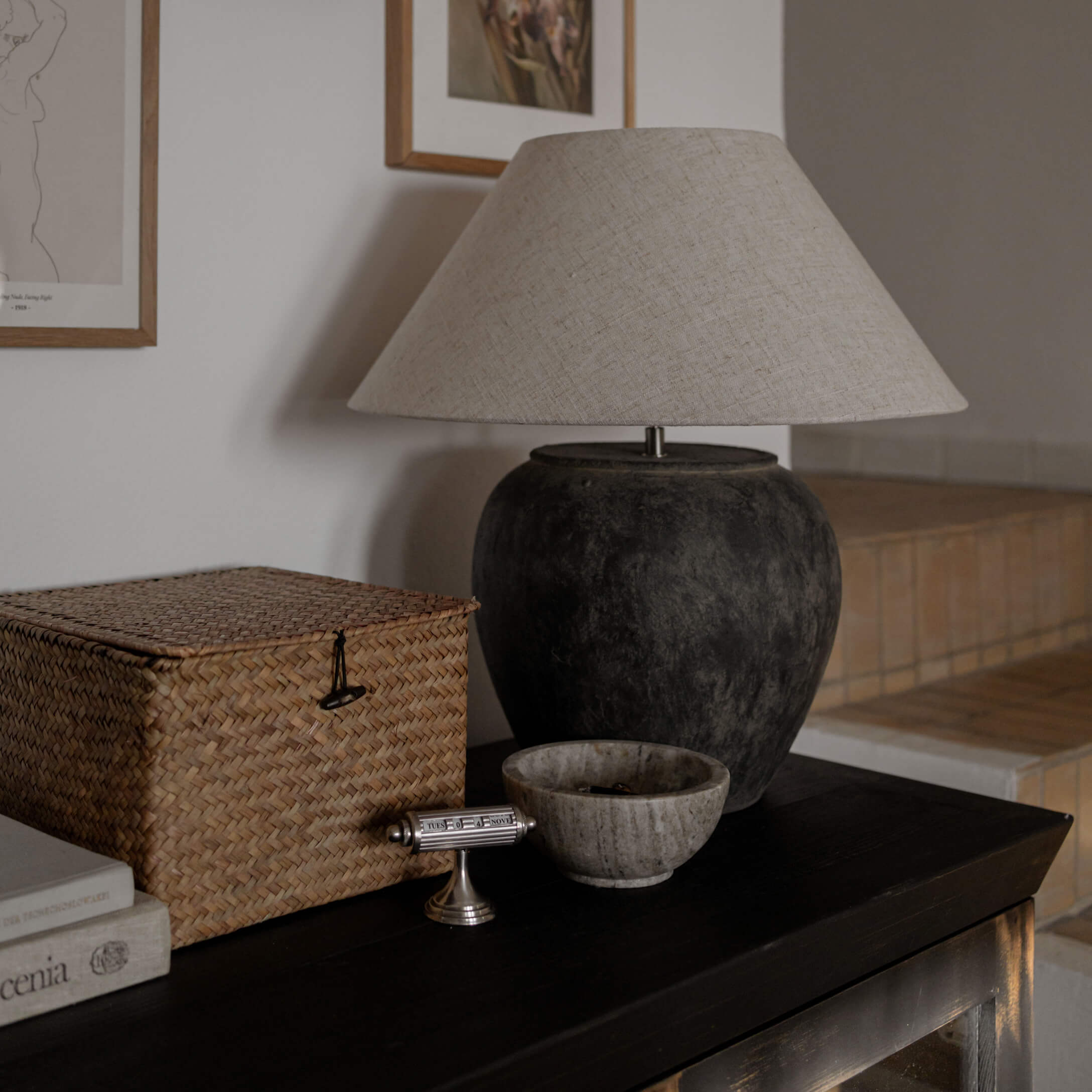 Stolní lampa s černou keramickou základnou a béžovým stínidlem na tmavém stole v obývacím pokoji