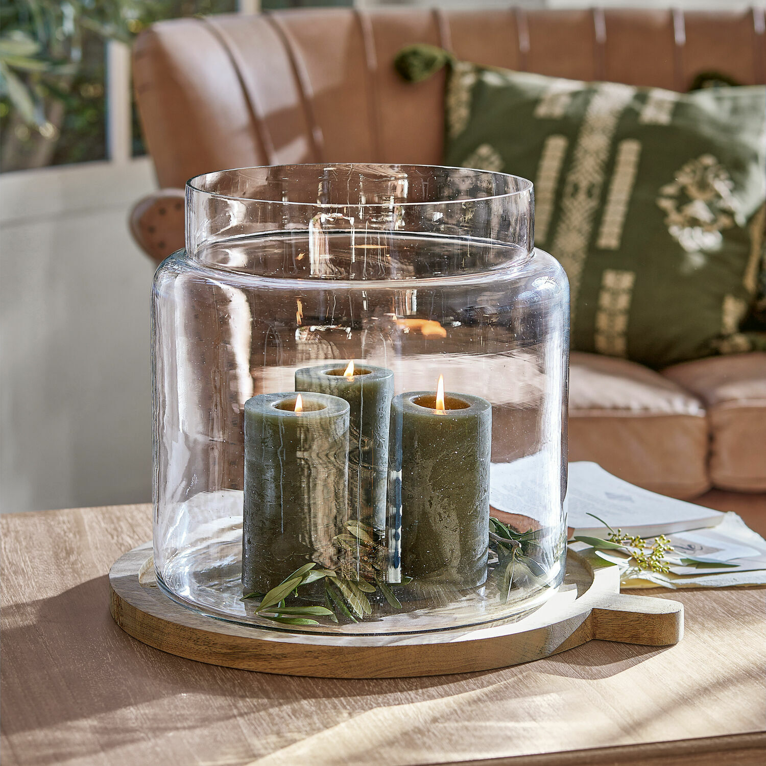 Skleněný svícen s třemi zelenými svíčkami na dřevěném podstavci na stole v obýváku
