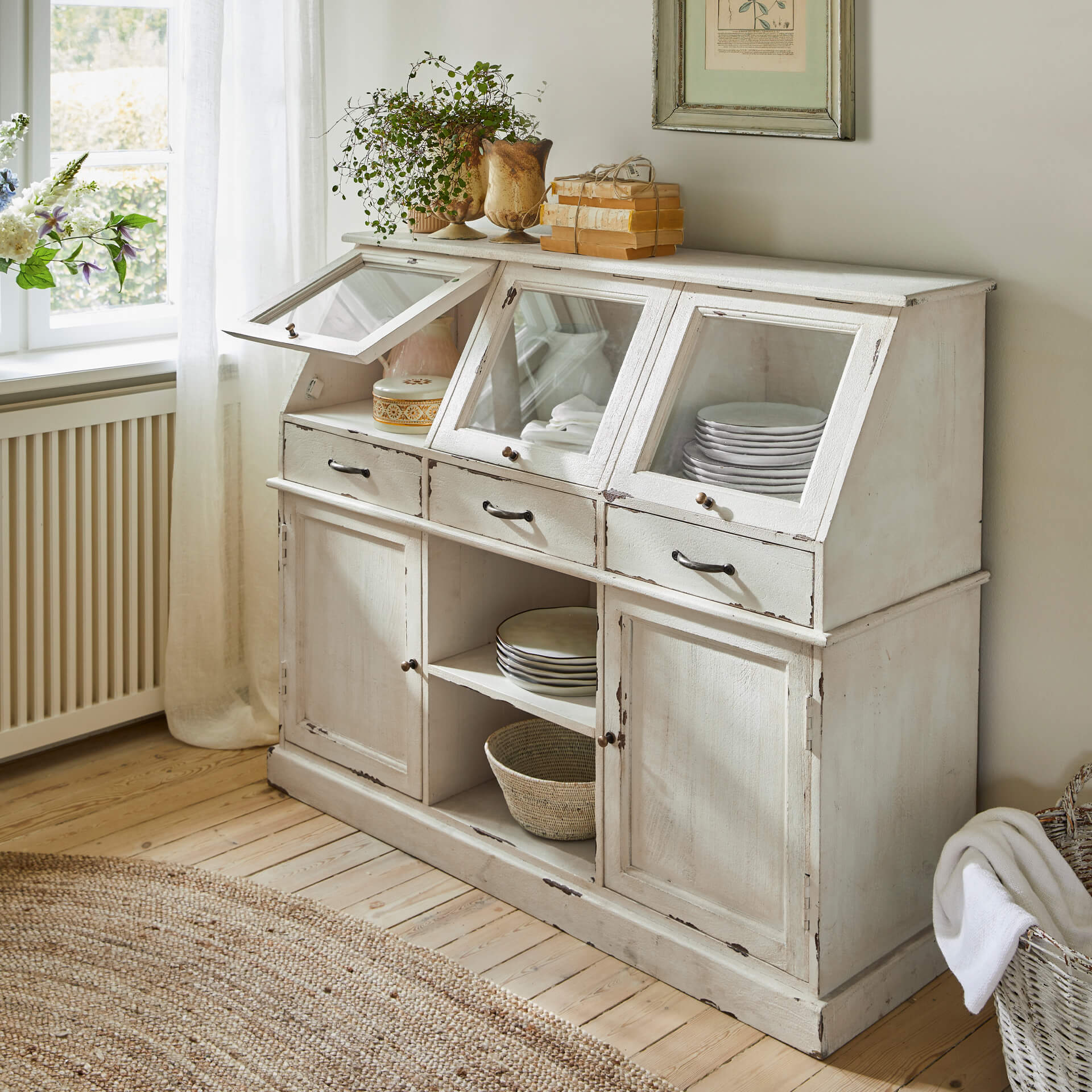 Bílá dřevěná kredenc s prosklenými dvířky a zásuvkami ve vintage stylu pro uložení nádobí